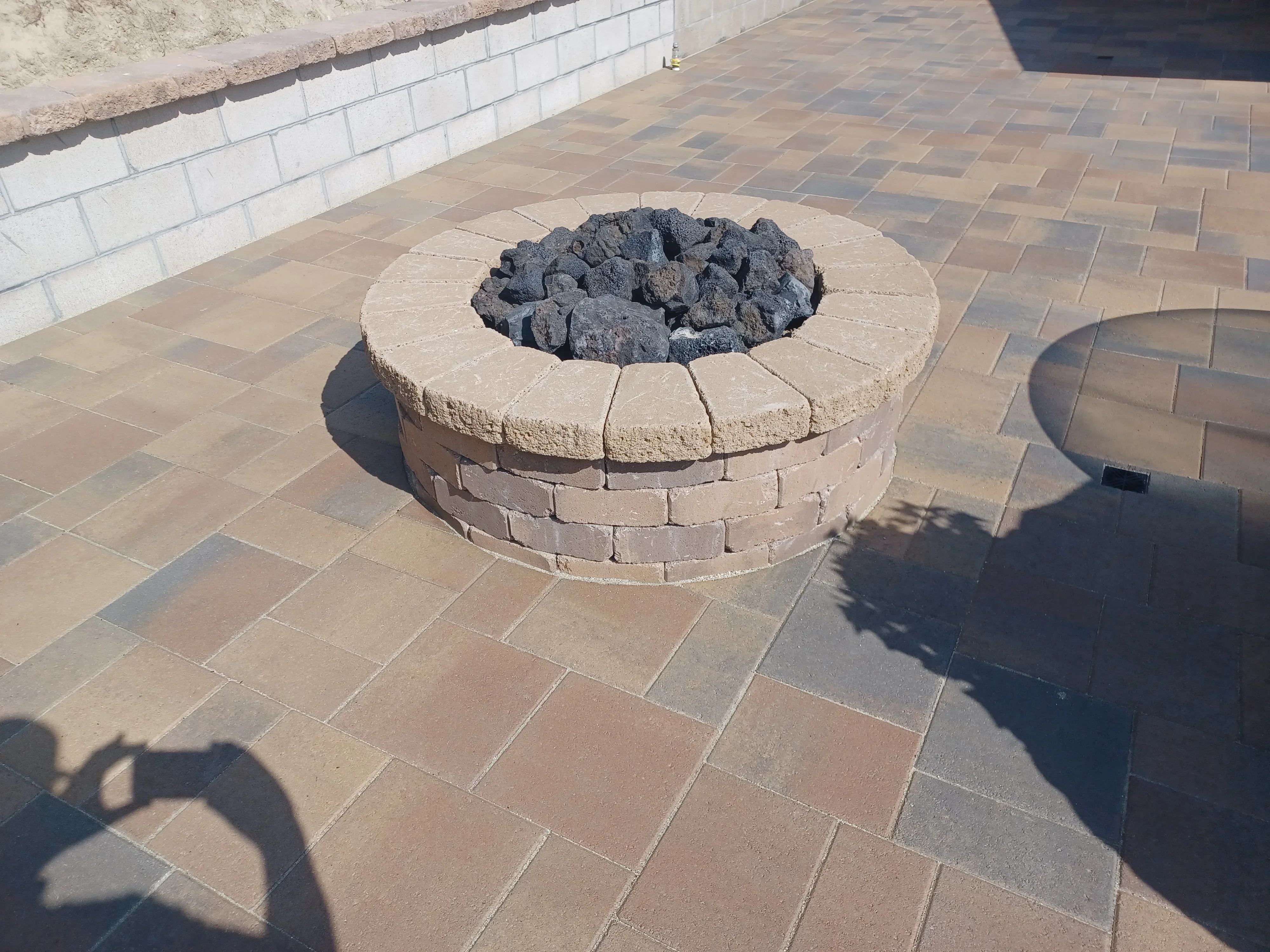 Circular fire pit with tan block walls and lava rock, surrounded by herringbone paver patio