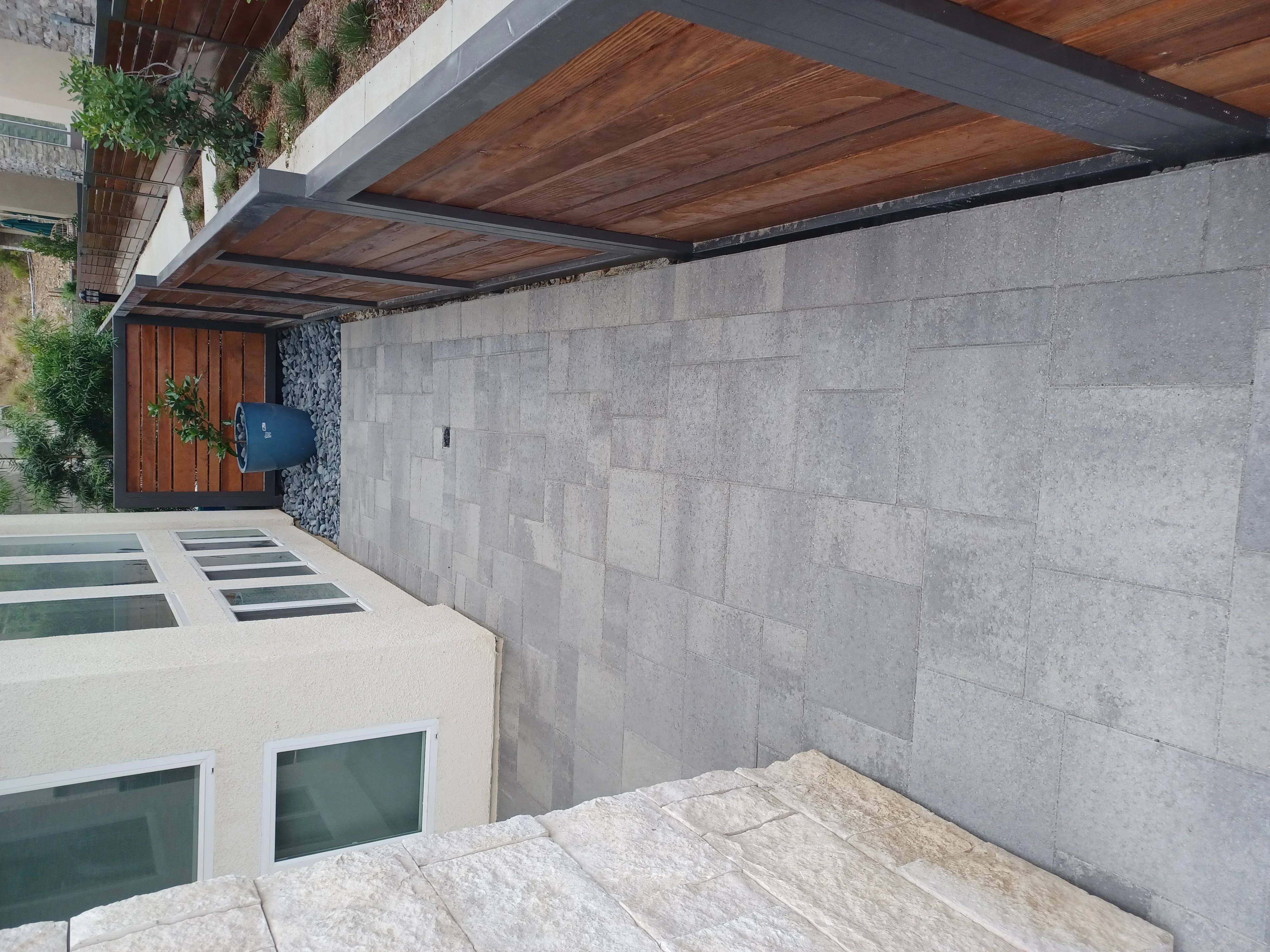 Concrete block retaining wall with wood pergola, paver patio, and modern home entry