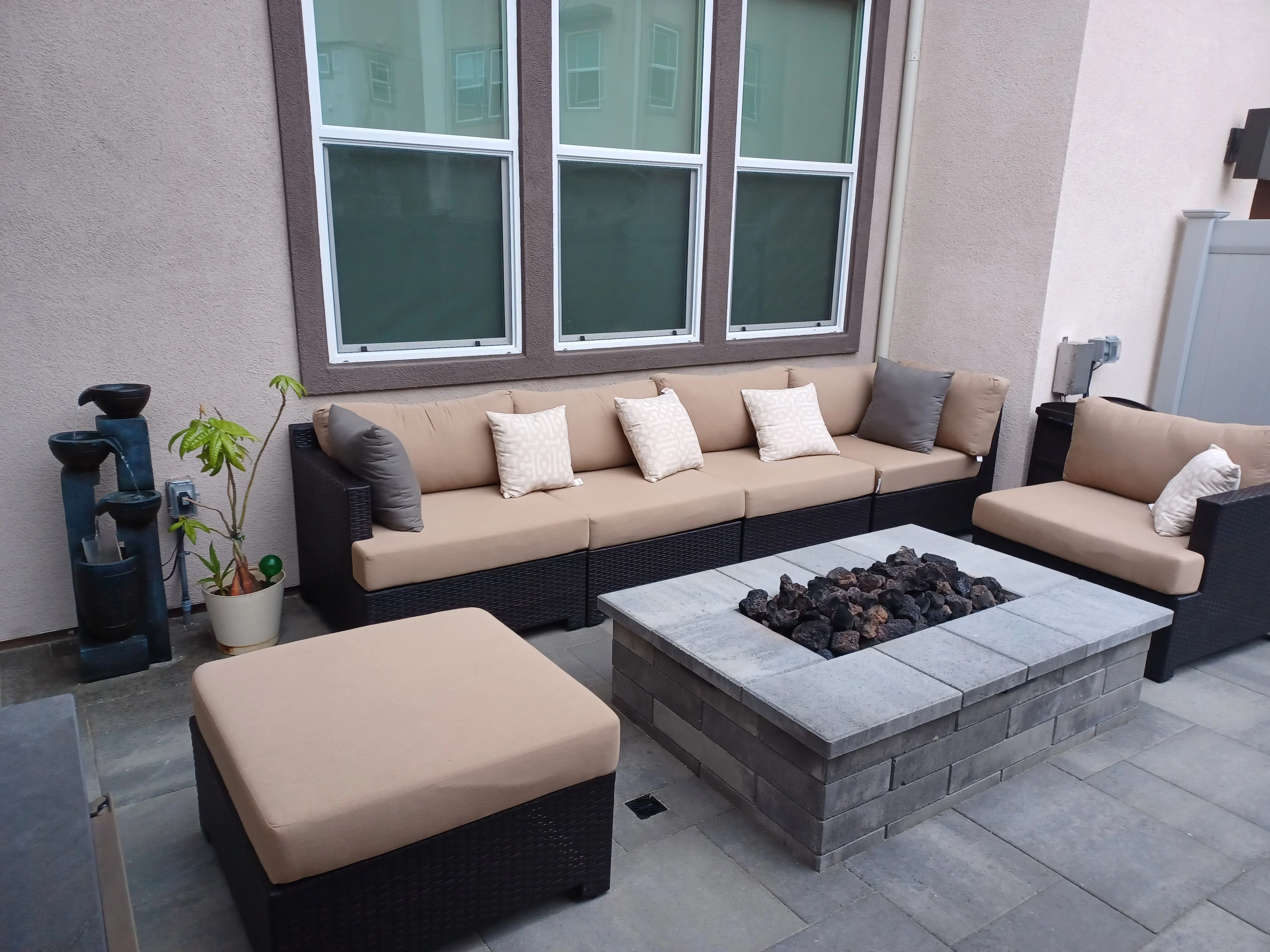Stone fire pit with gray cap and dark brick base on paved patio with wicker seating