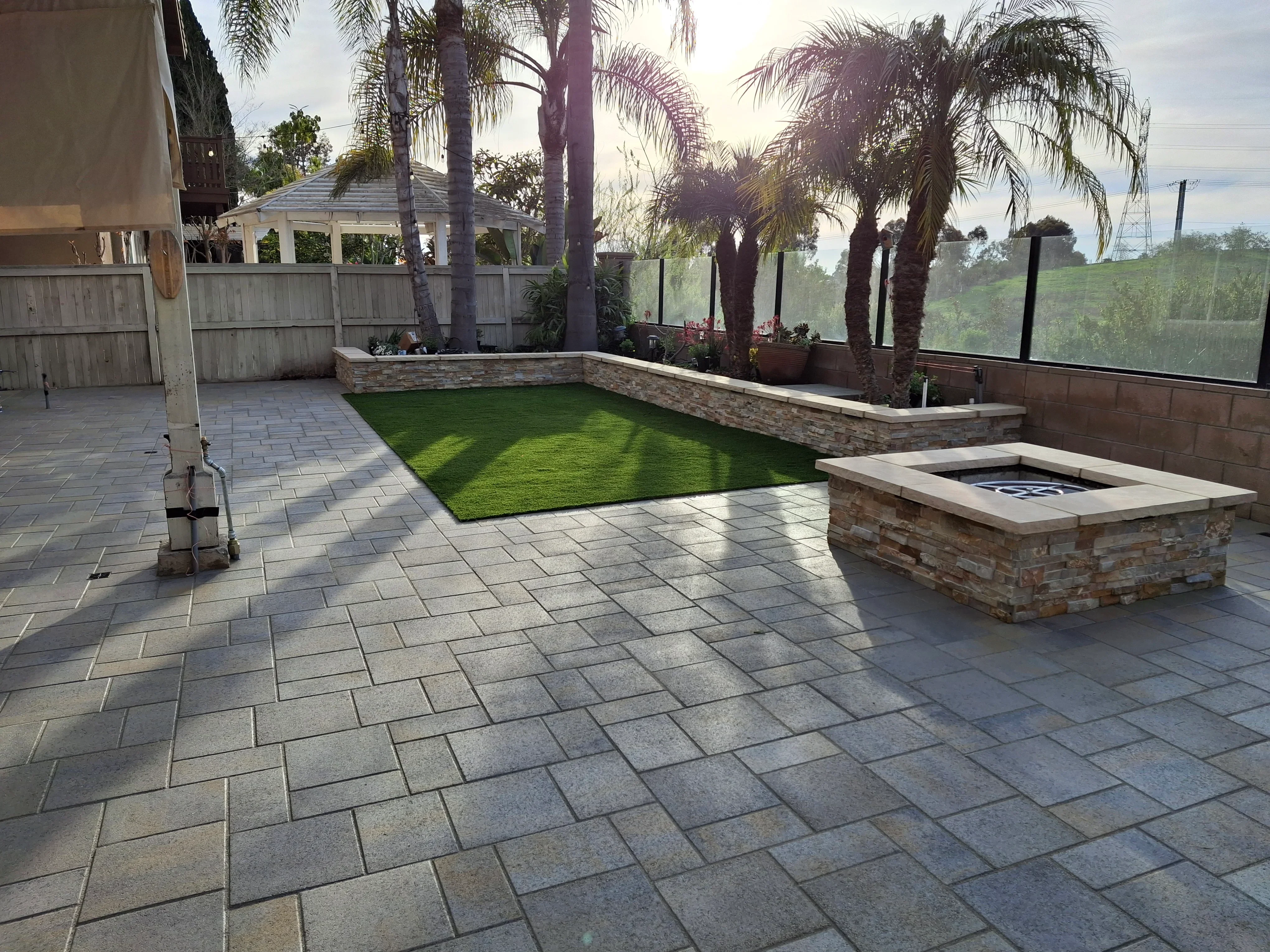Gray concrete paver patio with stone-veneer fire pit and raised planter beds