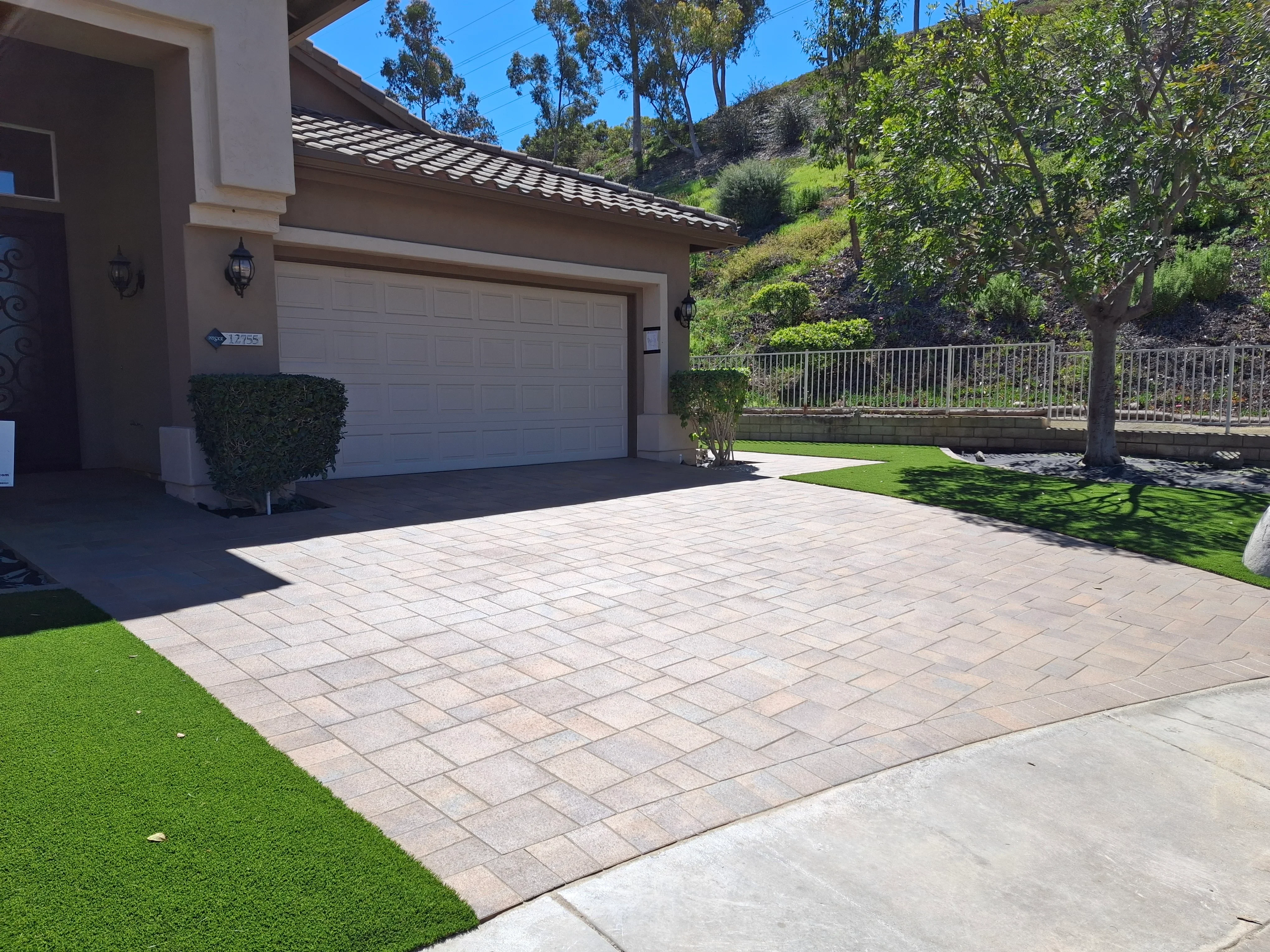 Permeable paver driveway with running bond pattern, synthetic turf borders, and metal railing