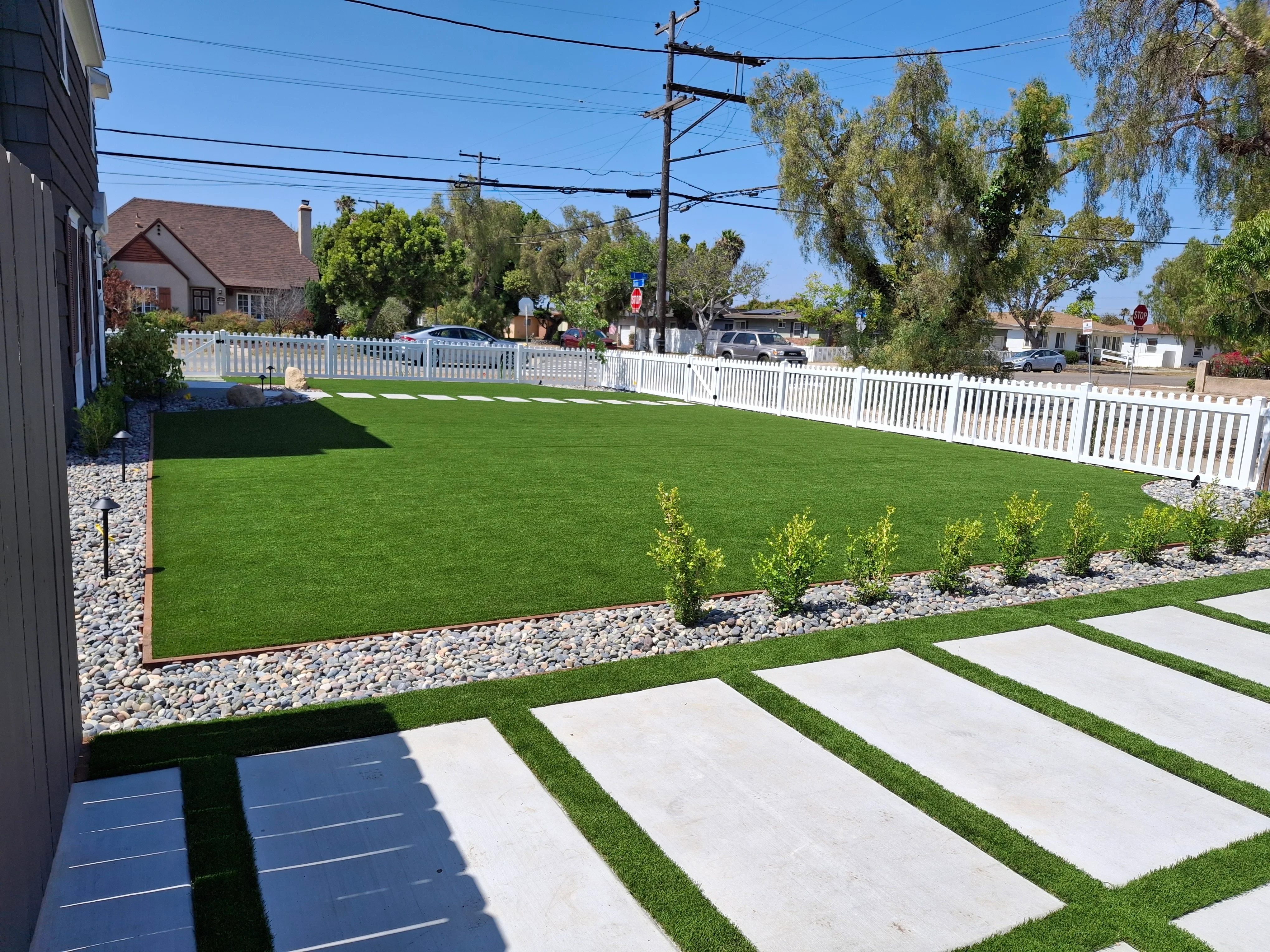 Synthetic turf lawn with concrete pavers, white vinyl fence, and river rock landscaping
