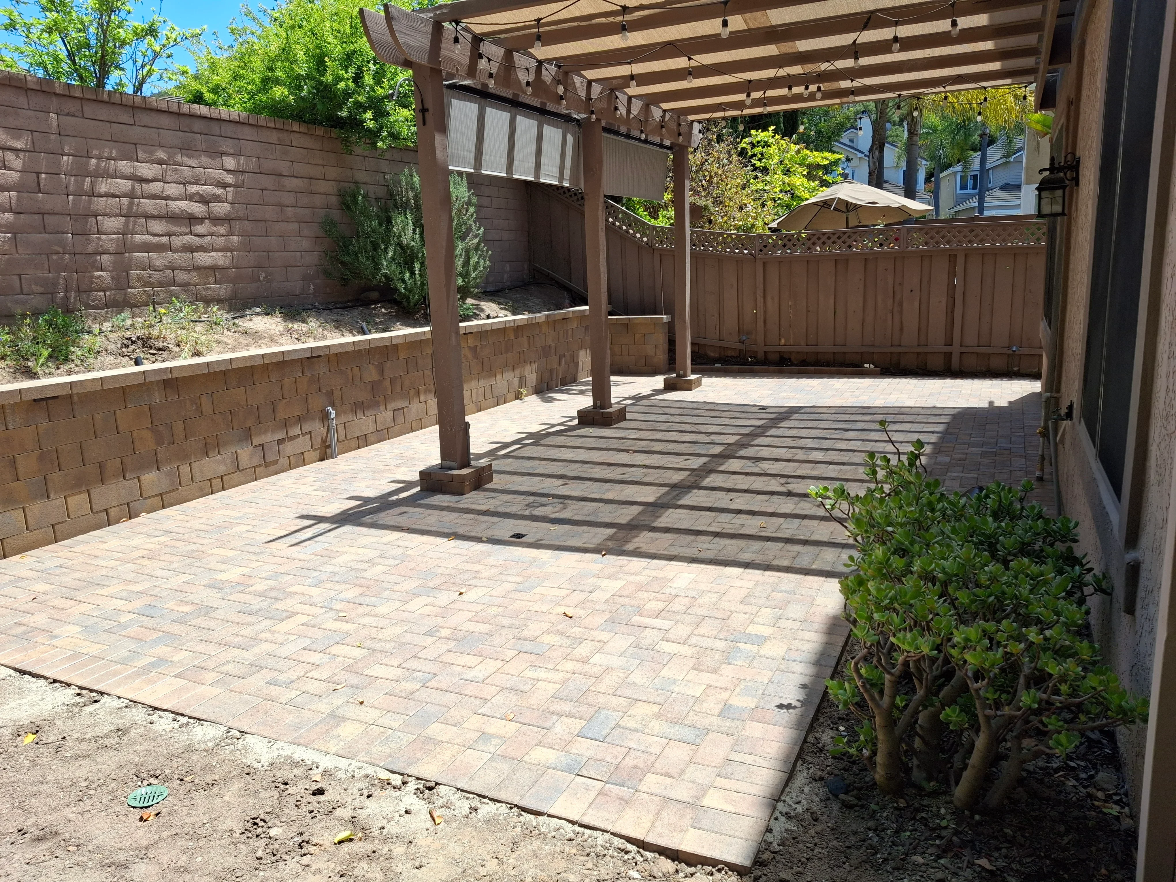 Clay brick paver patio with wood pergola, retaining walls, and lattice fence