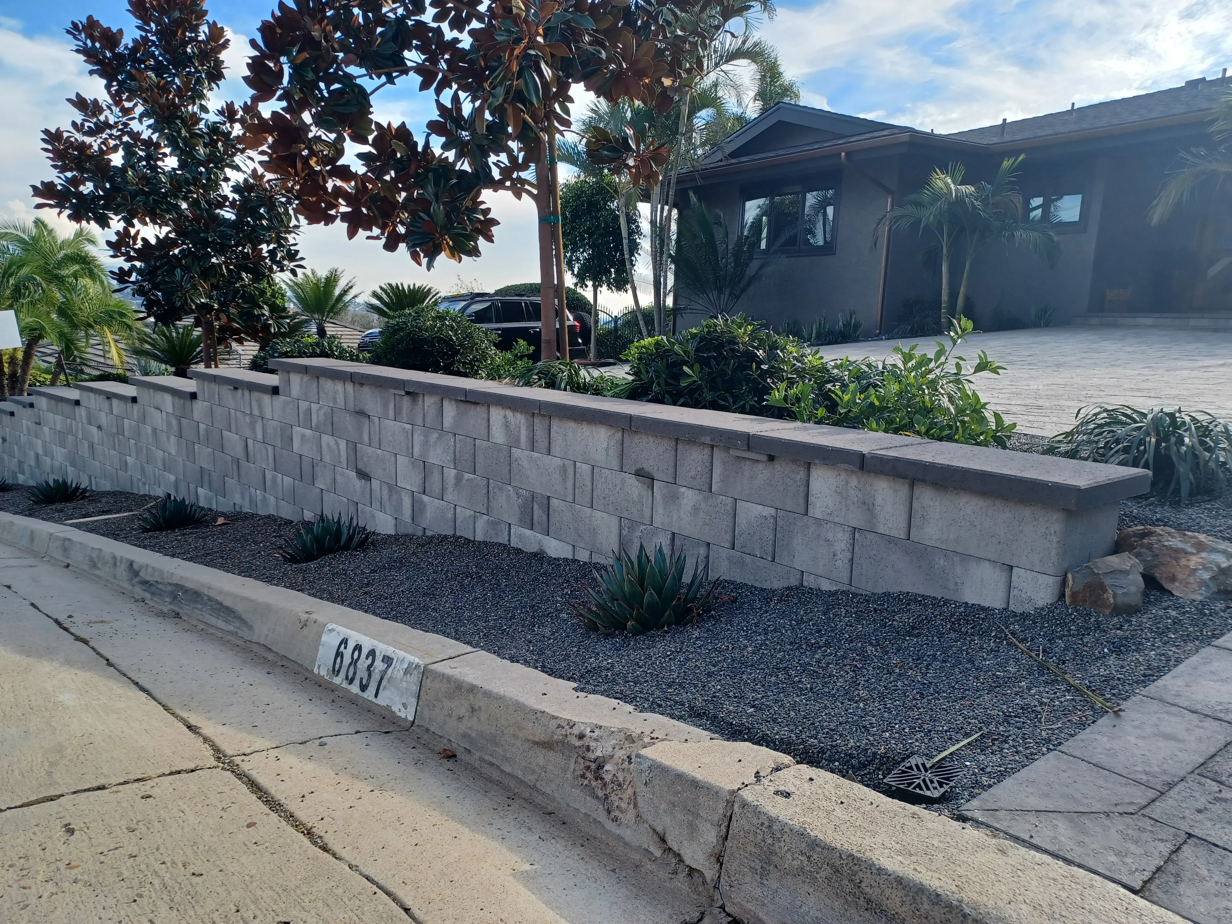 Concrete block retaining wall with cap stone, black rock mulch, and agave plantings