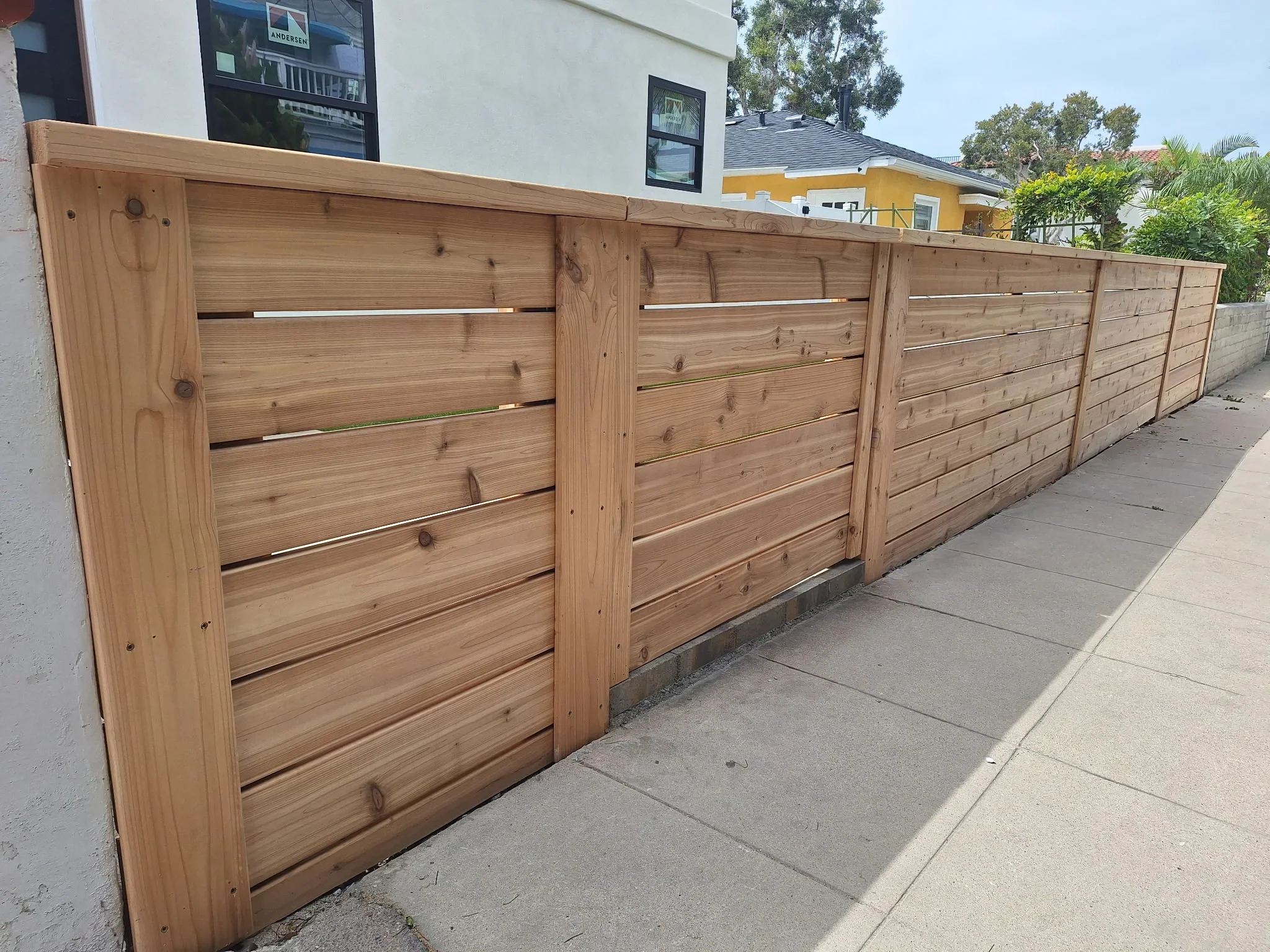 Horizontal cedar wood fence with metal accent strips and timber posts along driveway