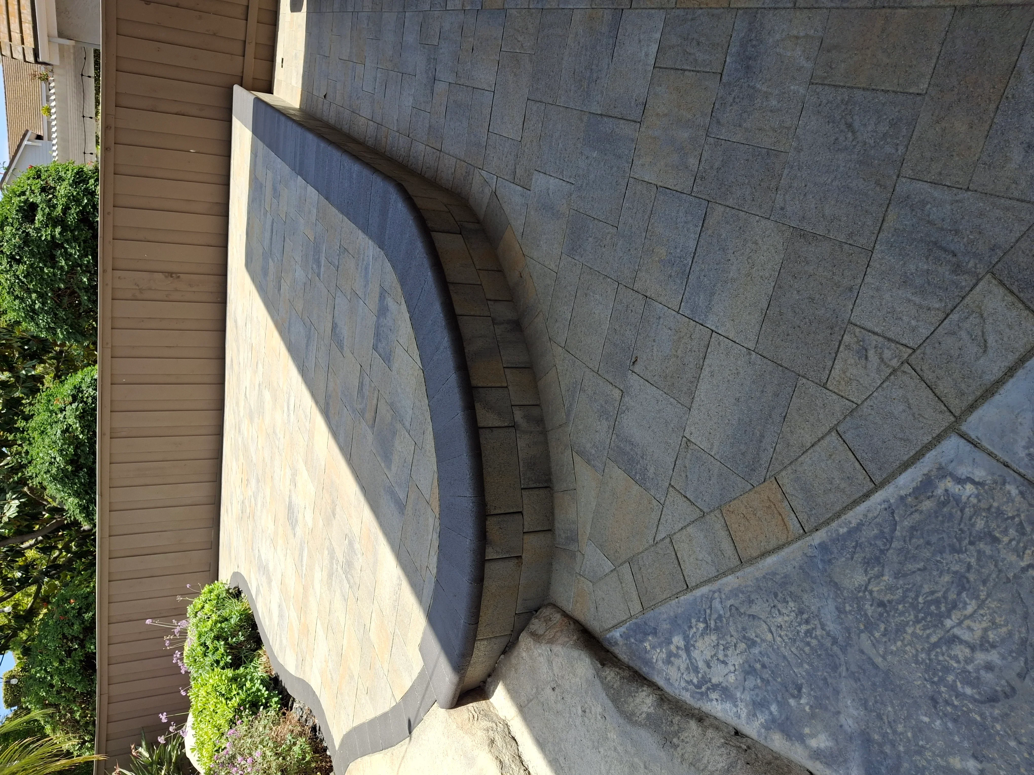 Curved gray paver patio with retaining wall and landscape edging