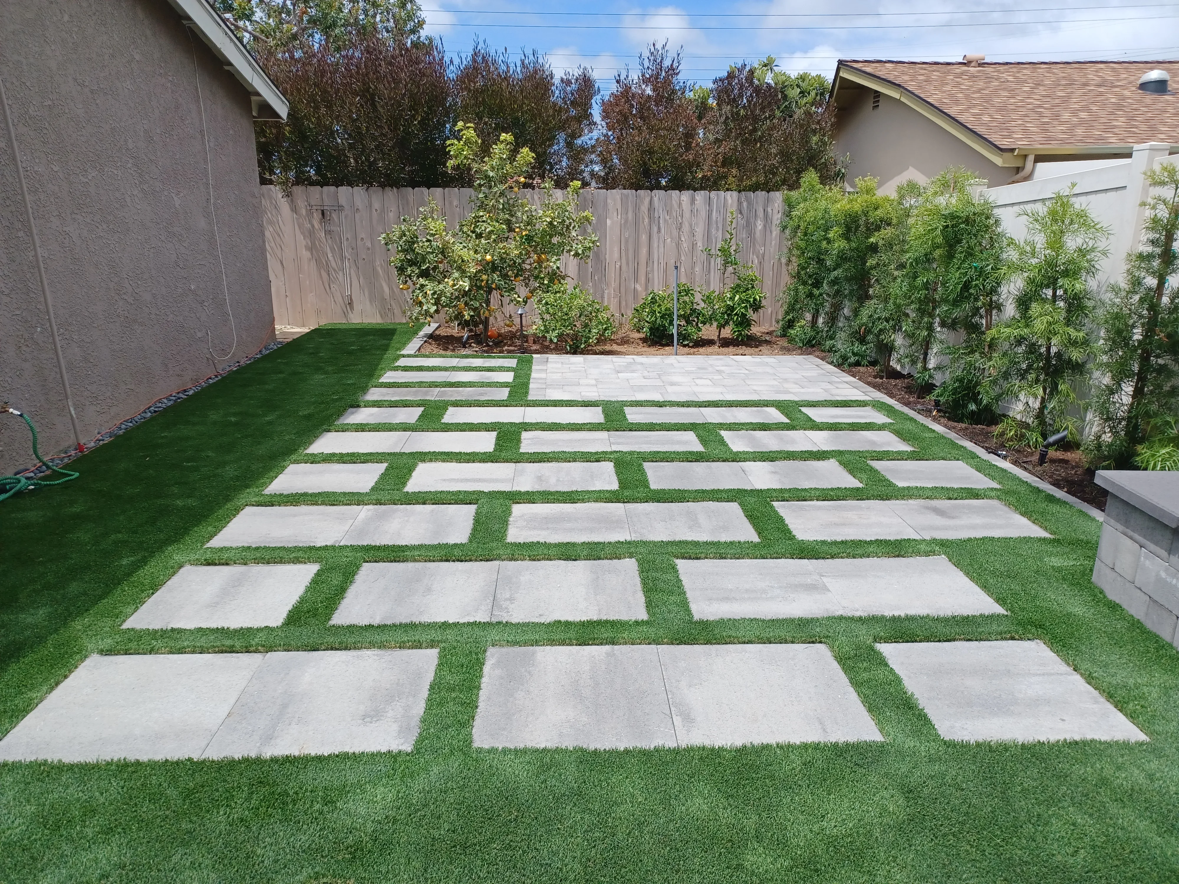 Concrete pavers with synthetic turf strips in geometric grid pattern through backyard