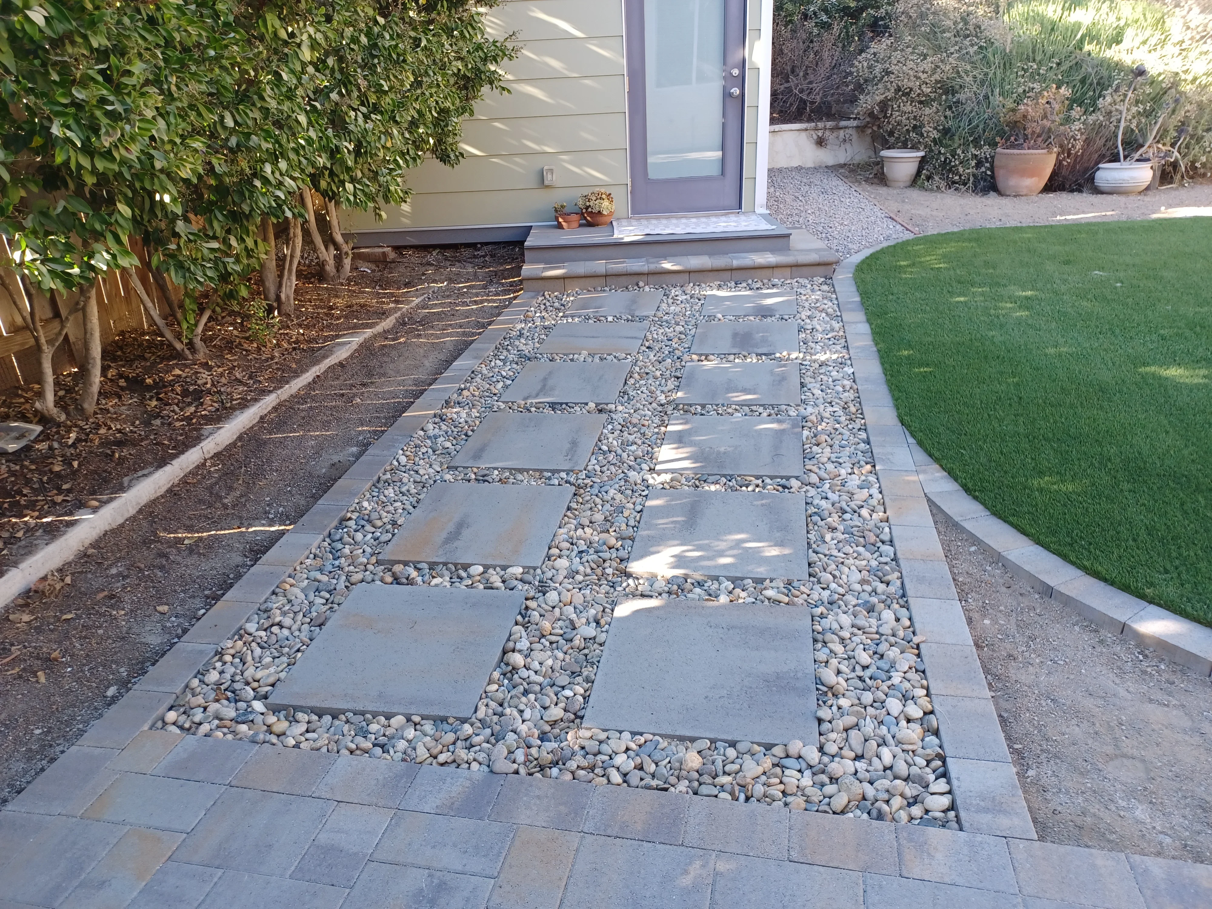 Gray concrete stepping stones with river rock infill and metal edging along pathway
