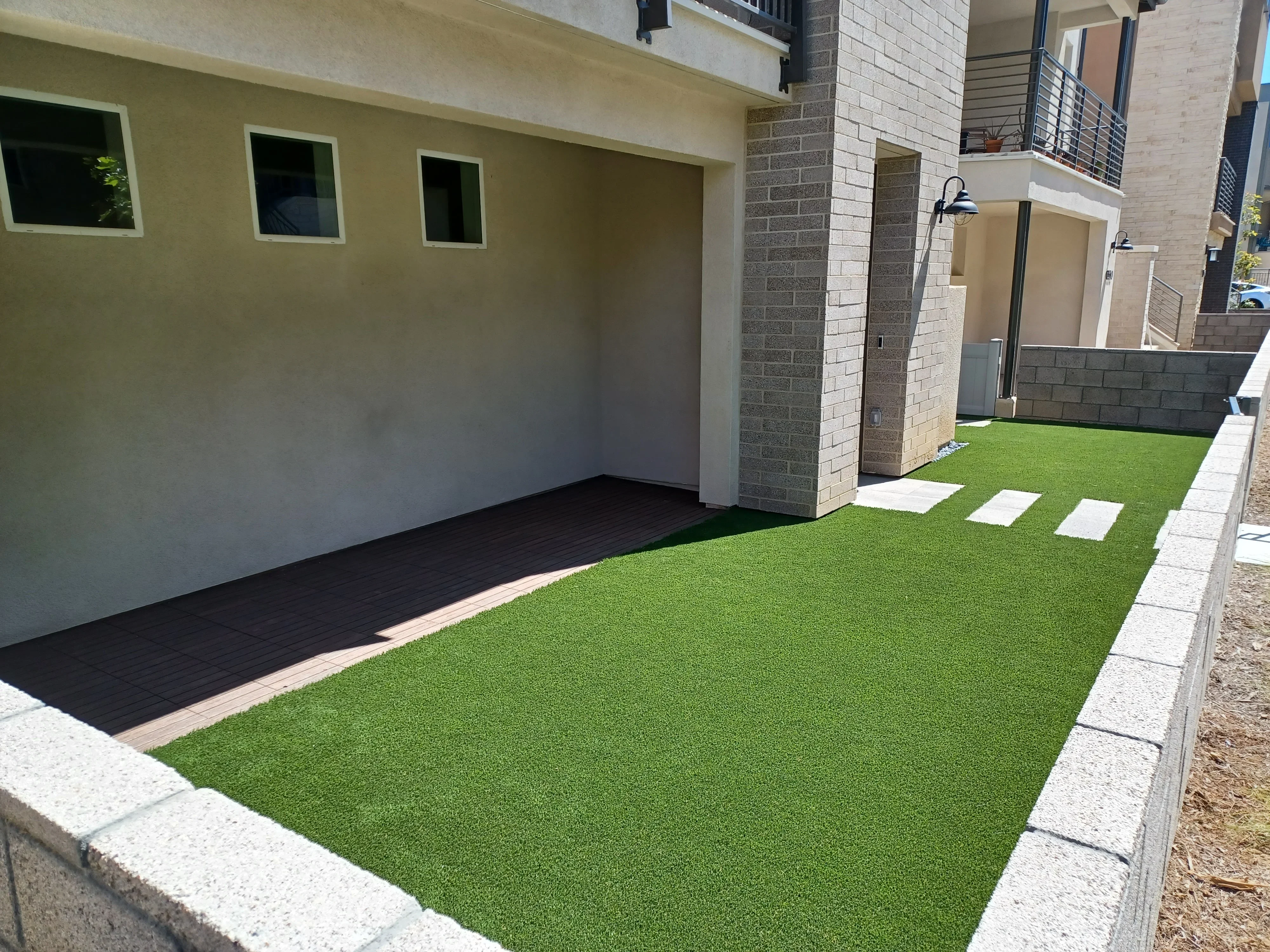 Synthetic turf courtyard with white stepping stones, black rubber mulch, and concrete edging