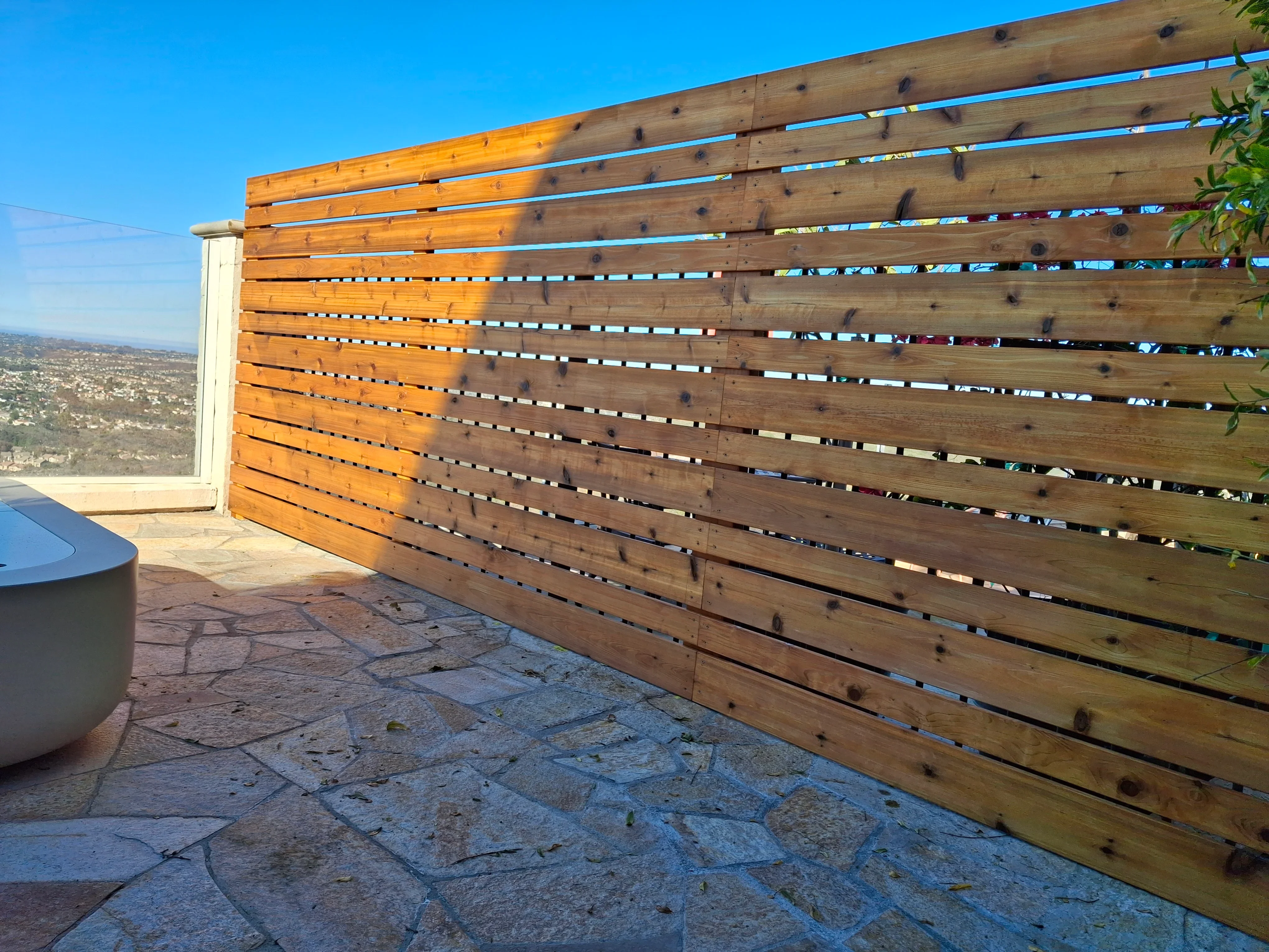 Horizontal wood slat privacy screen with metal accents on stone paver patio