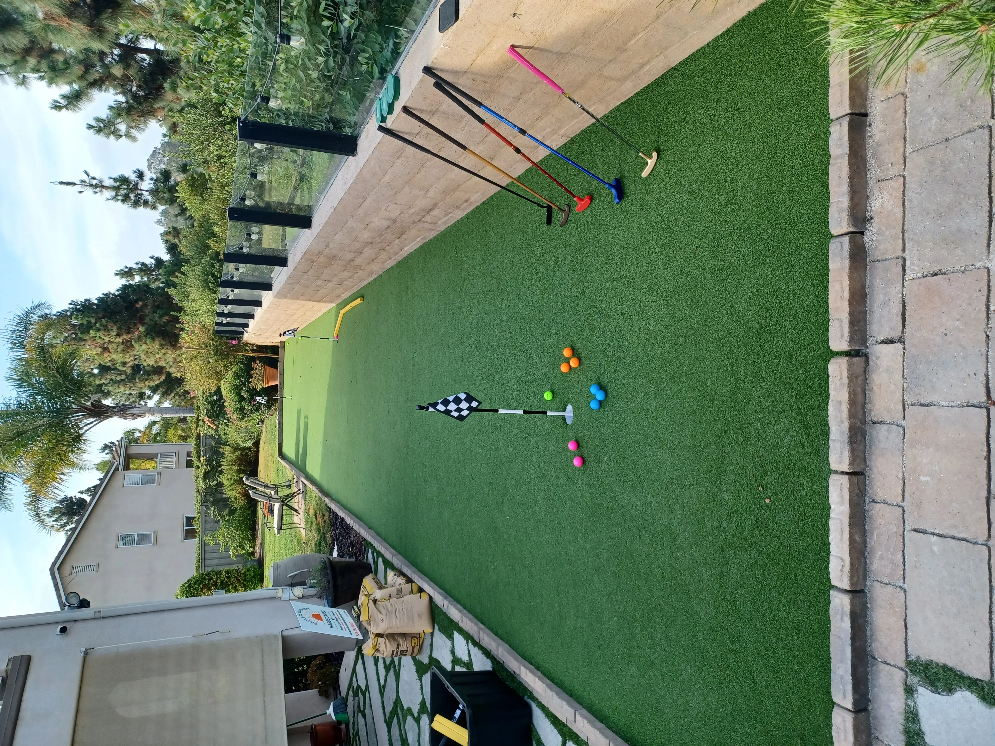 Synthetic turf putting green with practice holes, colored golf balls, and chipping clubs on concrete patio