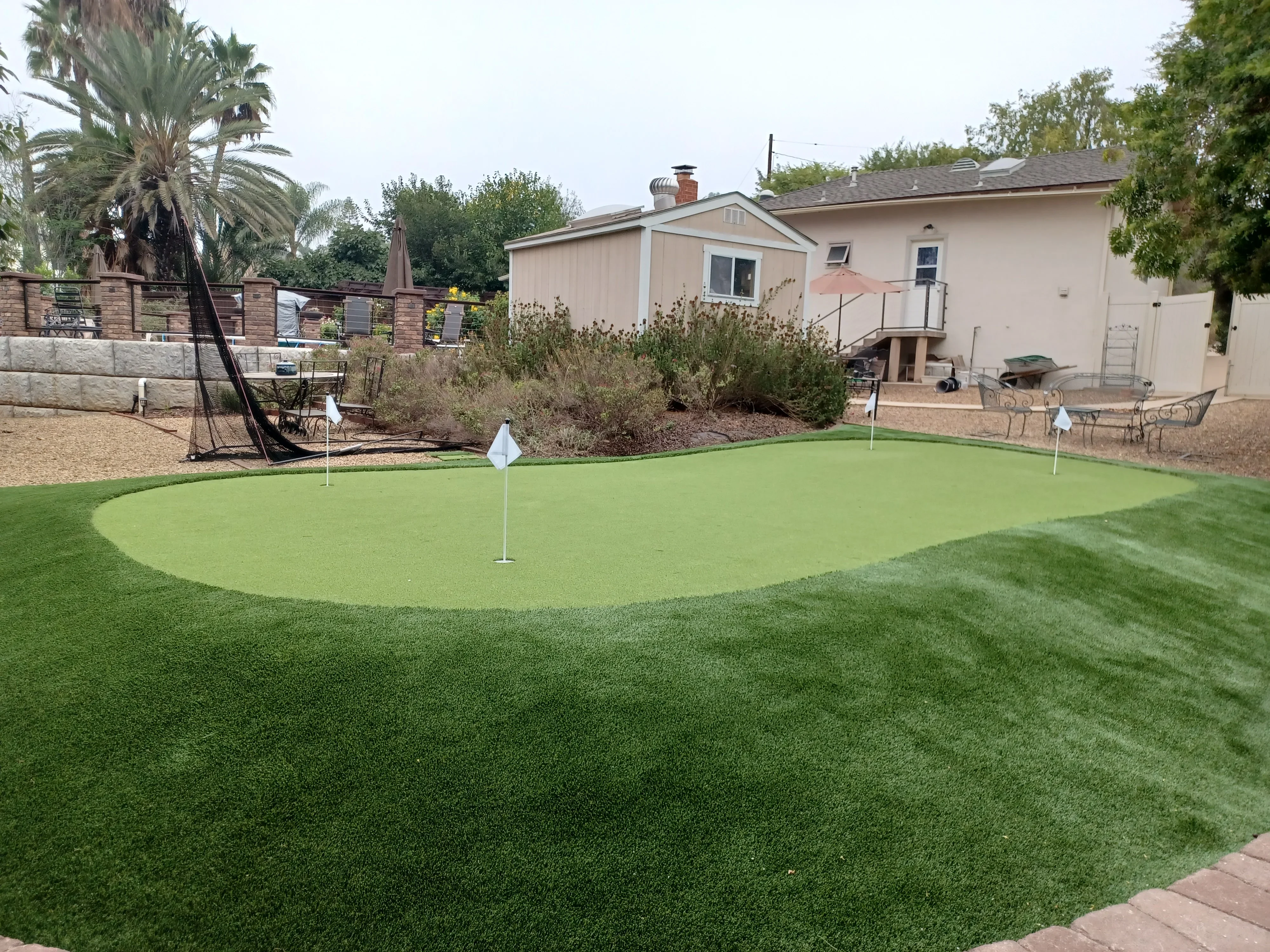 Synthetic putting green with fairway, hole markers, and brick patio in residential backyard