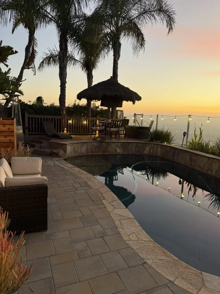 Large-format pavers, curved infinity pool, stone coping, and glass railings at sunset