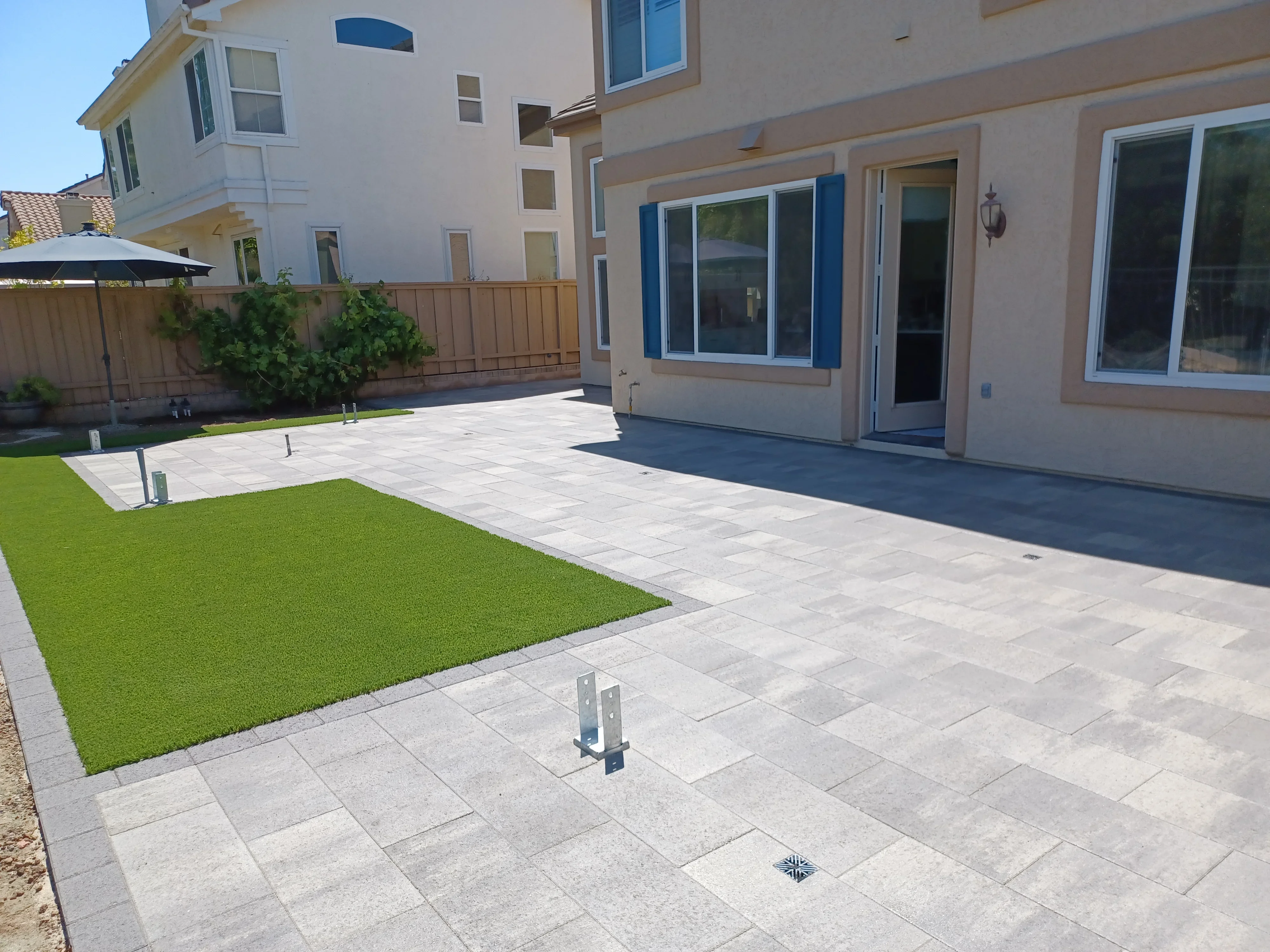 Concrete paver patio with synthetic turf, drainage system, and modern home exterior