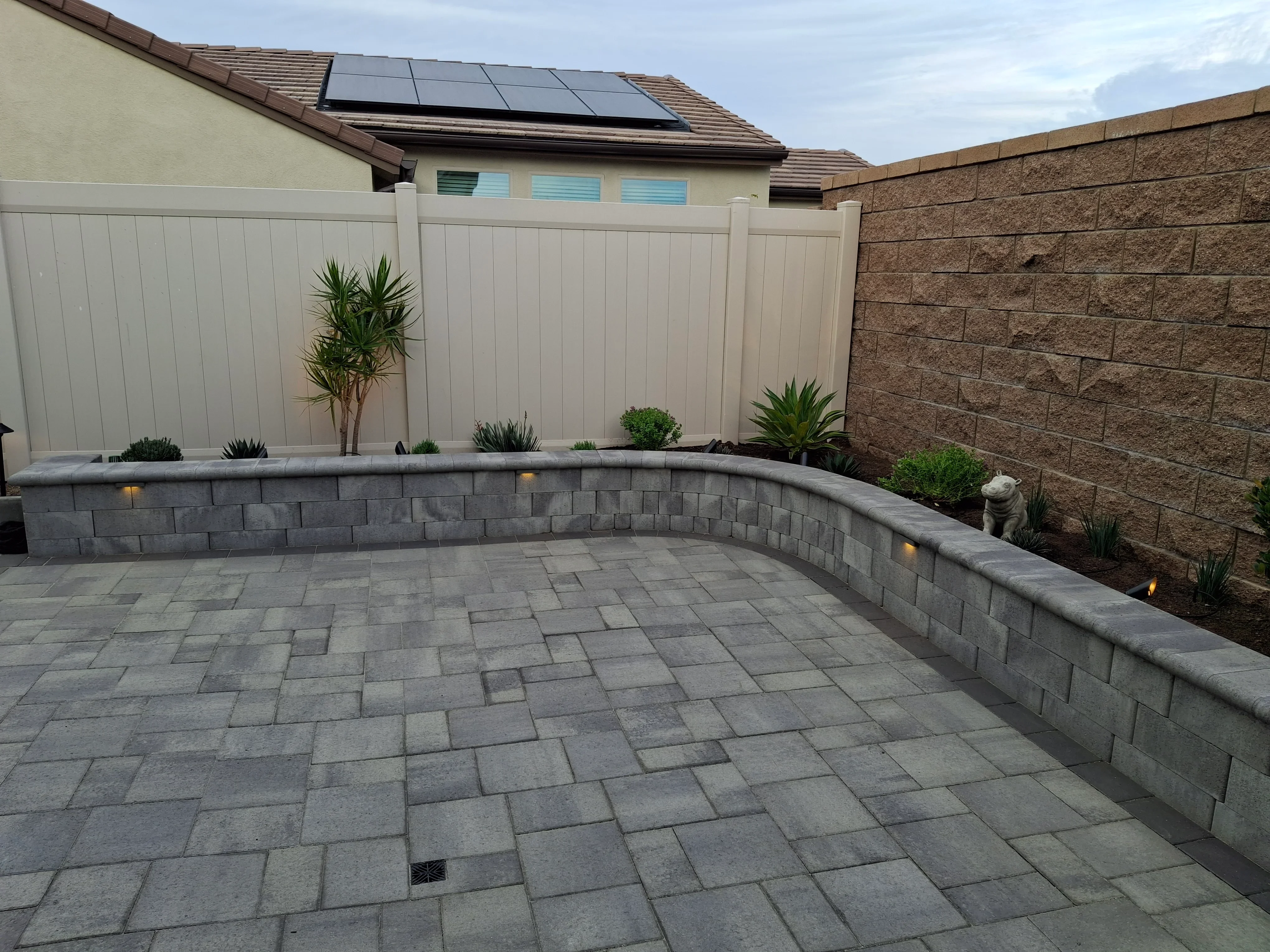 Gray concrete block retaining wall with cap stone and LED lighting, permeable paver patio in geometric pattern