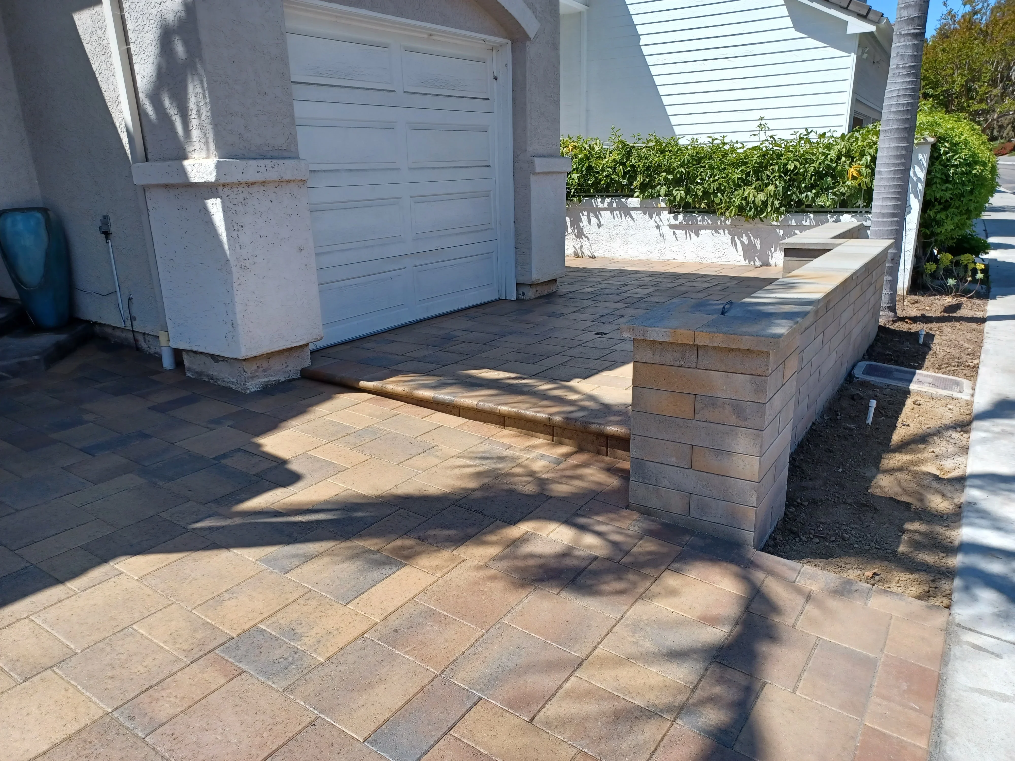 Tan and gray paver driveway with concrete block retaining wall and step