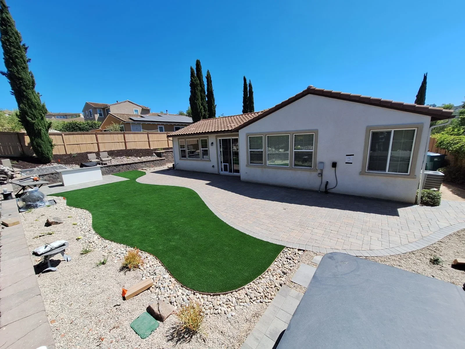 Curved paver patio with synthetic turf, river rock borders, and retaining wall installation