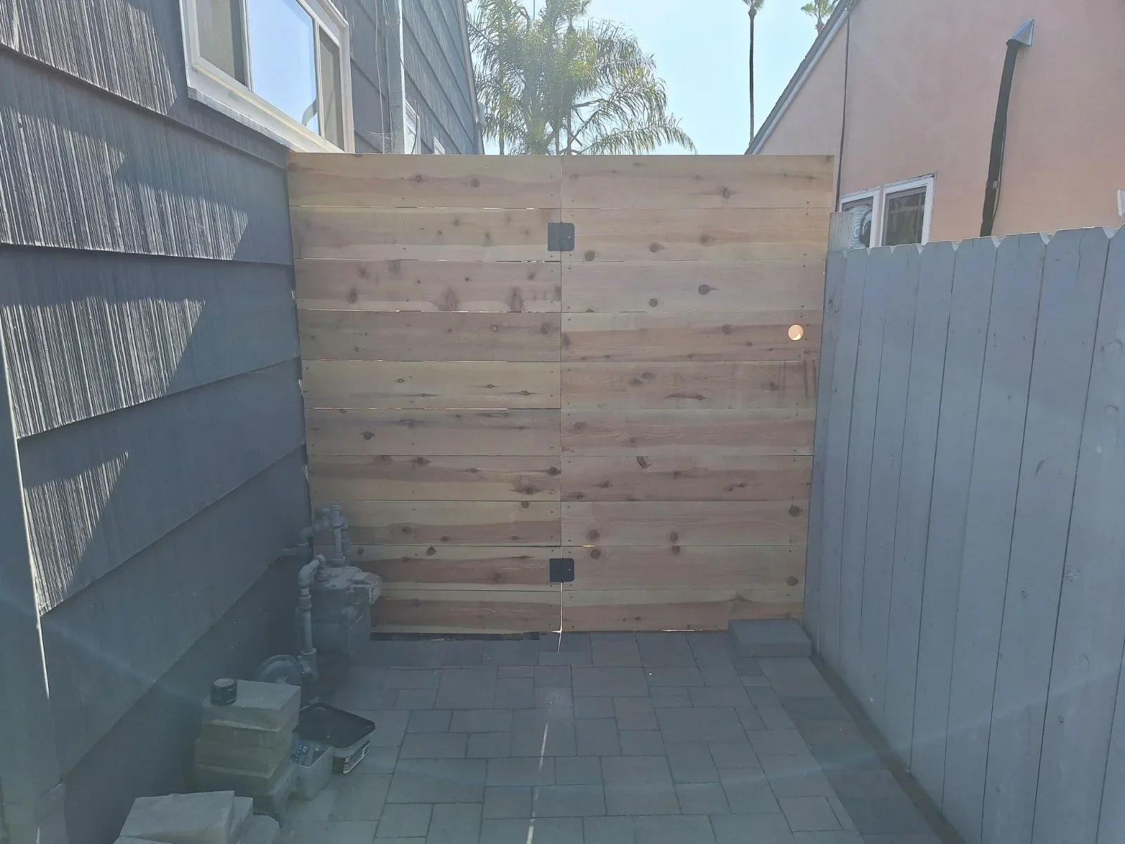 Horizontal cedar wood driveway gate with metal hardware in paved courtyard
