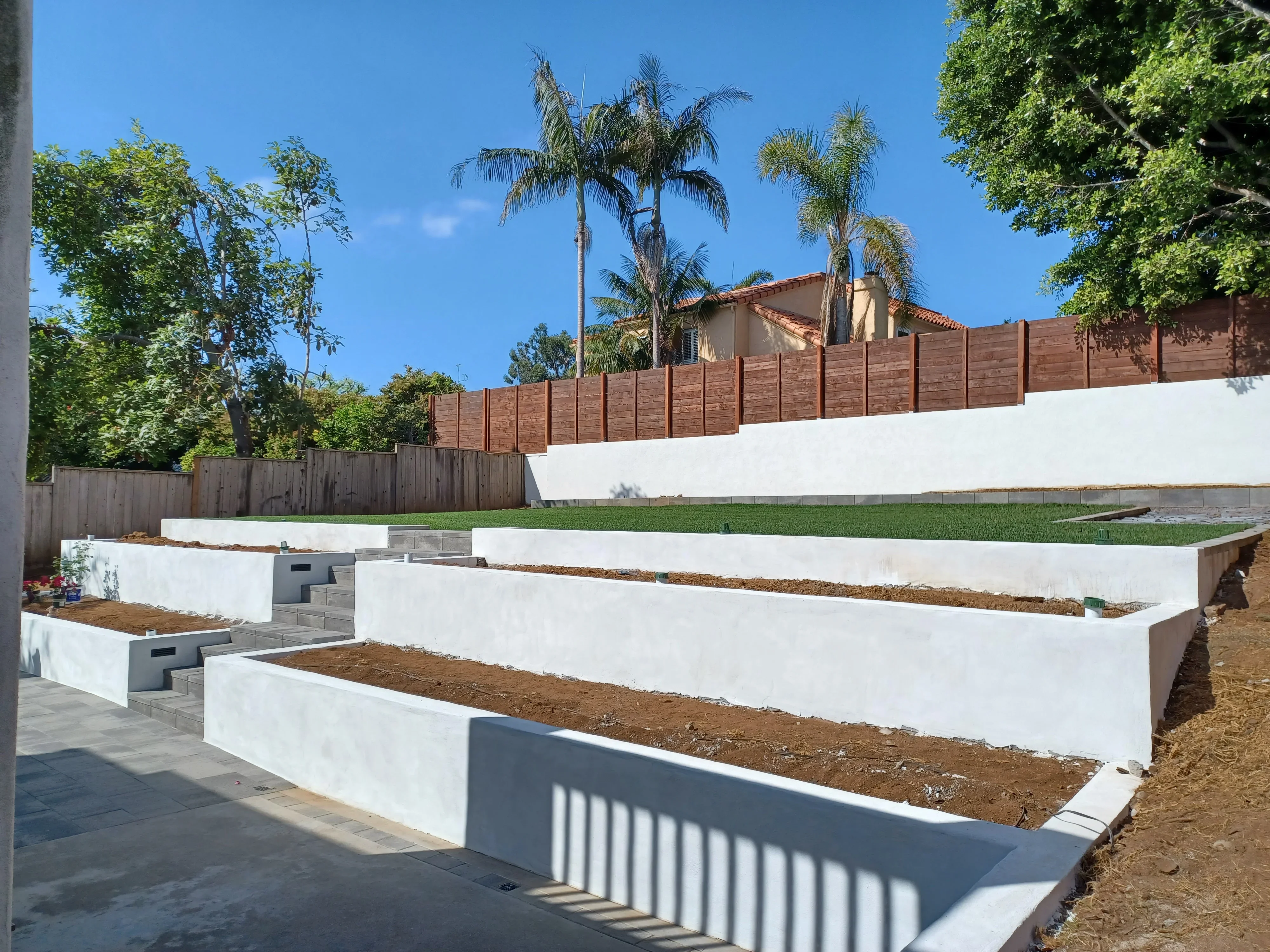 White concrete tiered raised garden beds with timber edging and concrete block steps on sloped yard