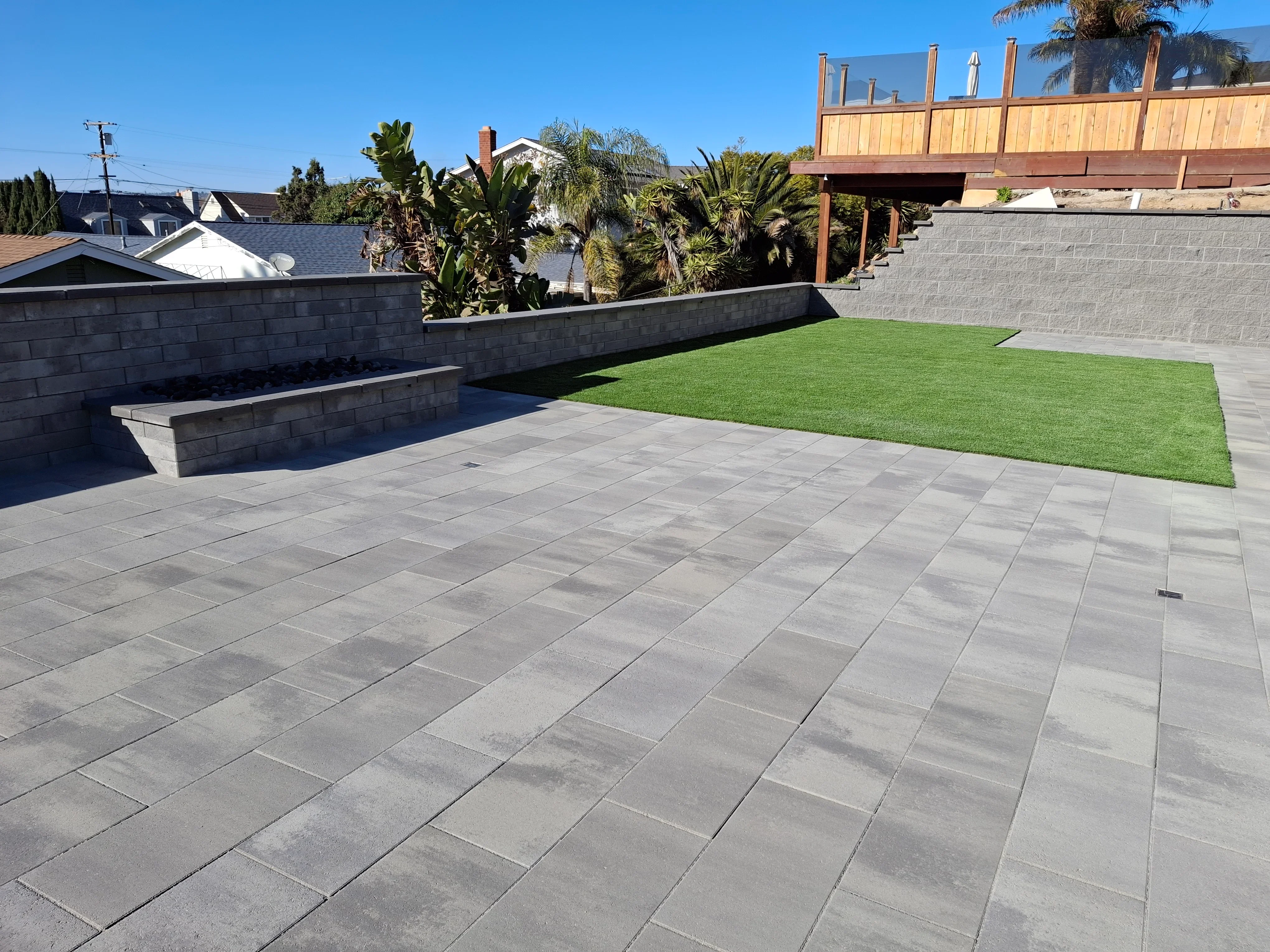 Gray porcelain paver patio with concrete retaining walls, raised planters, and synthetic turf lawn