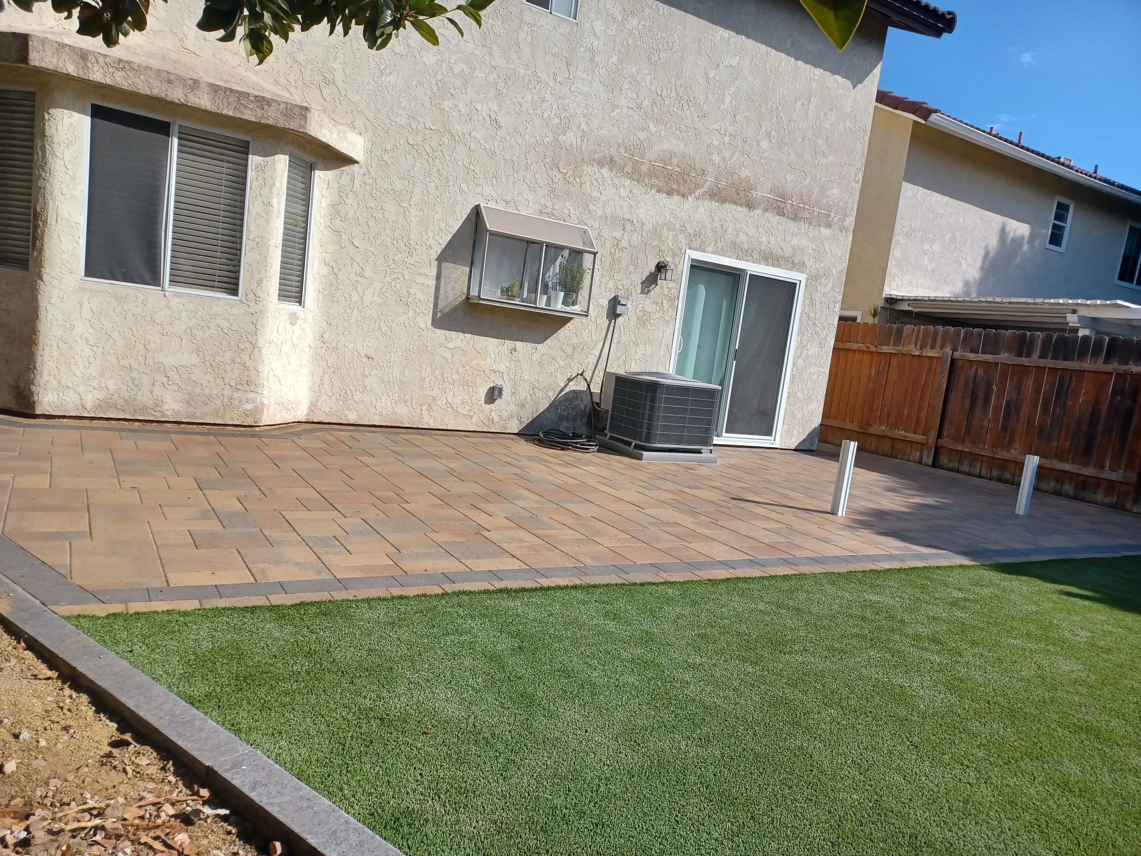 Clay paver patio with synthetic turf and concrete edging bordering residential home