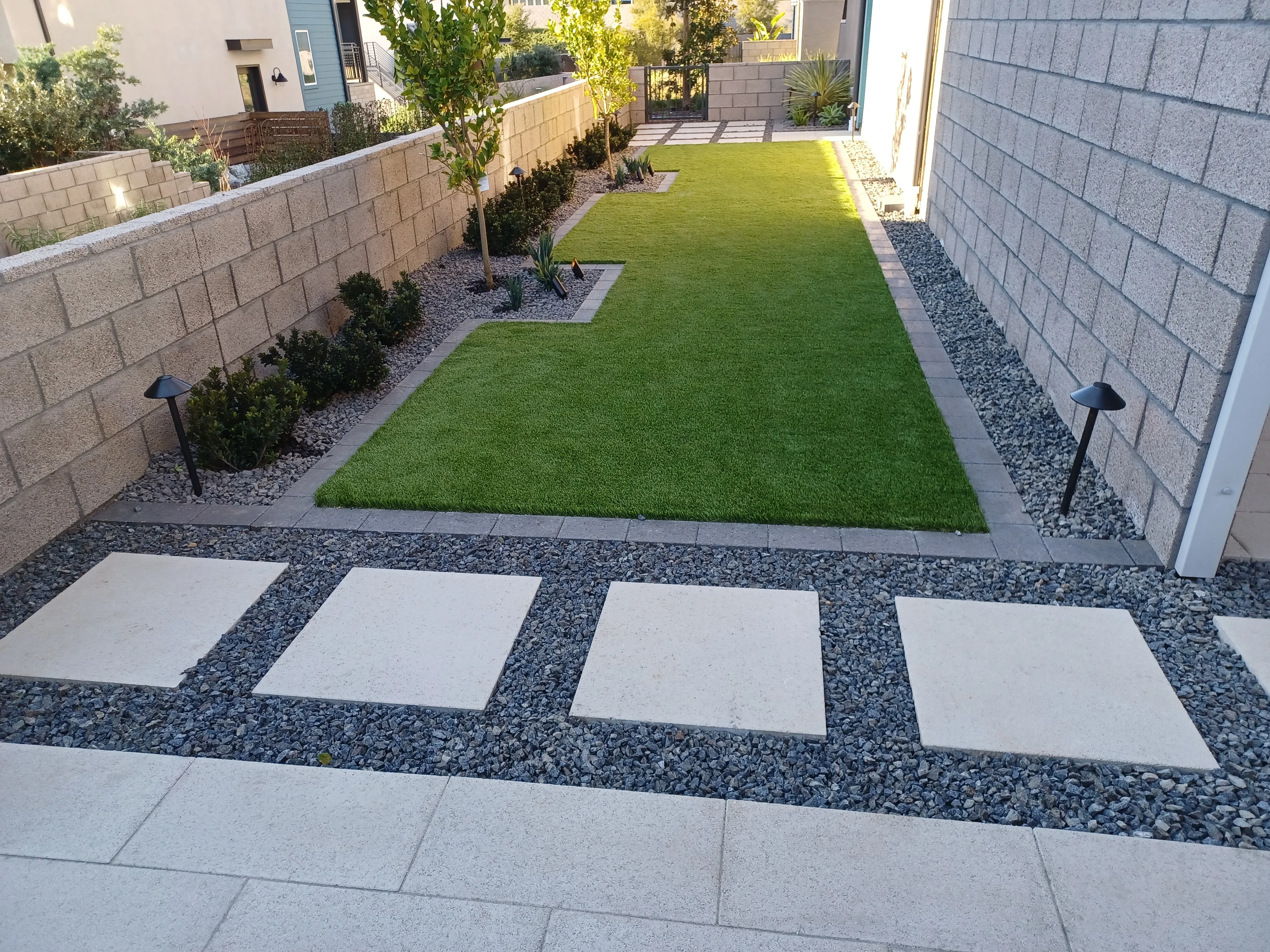 Synthetic turf lawn with concrete stepping stones, river rock, and concrete block retaining walls