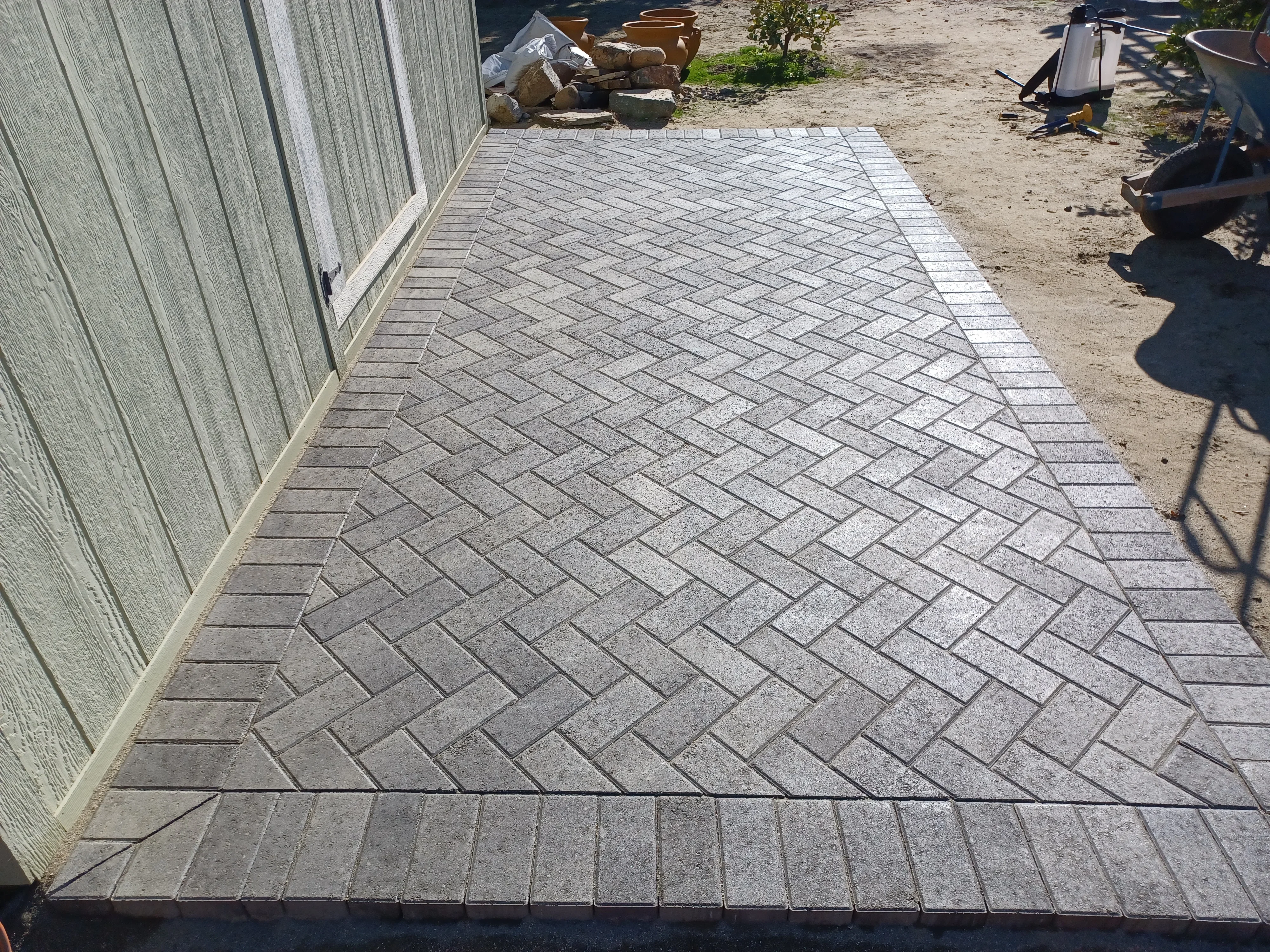 Gray concrete pavers laid in herringbone pattern with border detail along building edge
