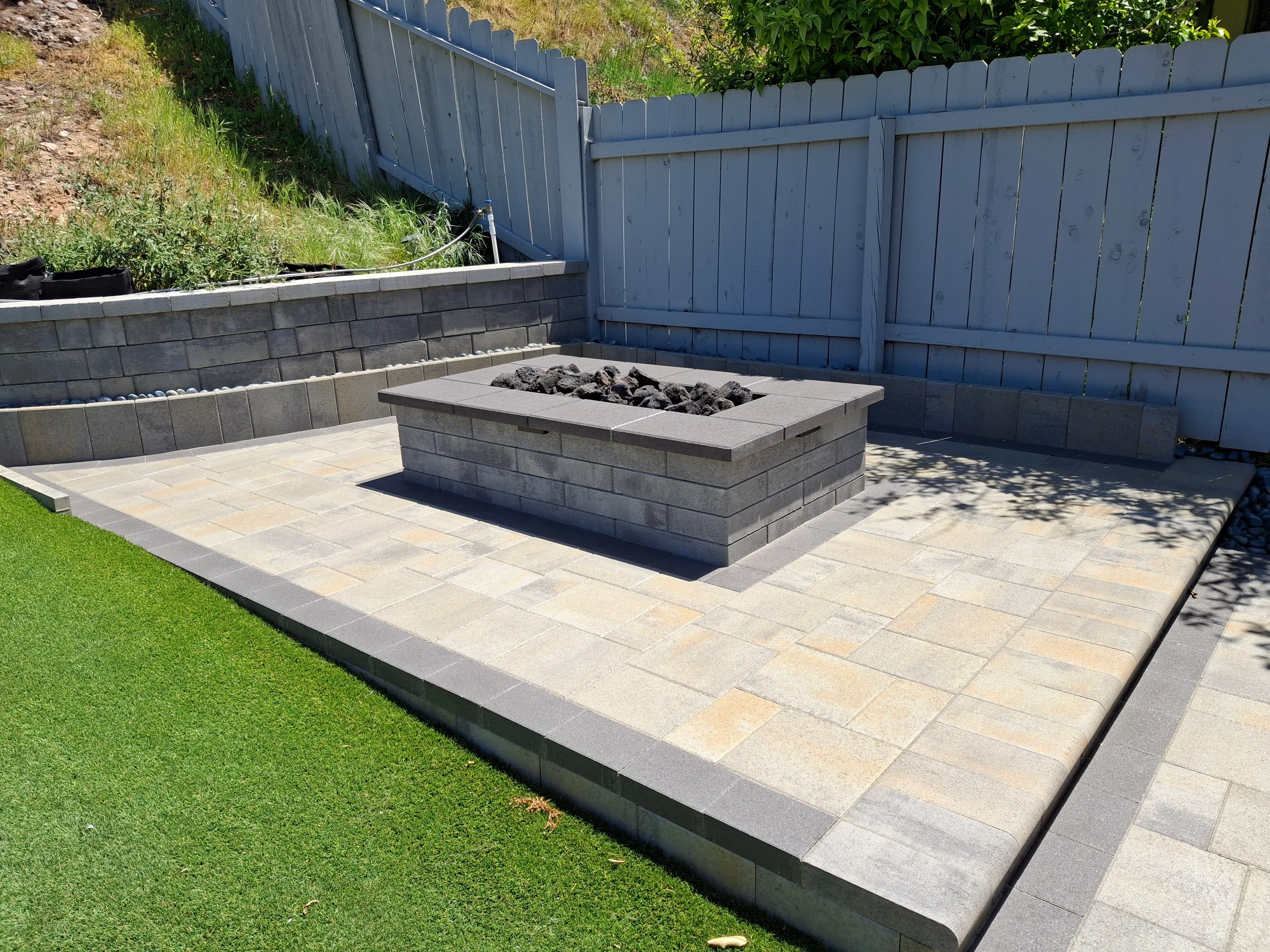 Tan paver patio with gray block fire pit and retaining wall in backyard