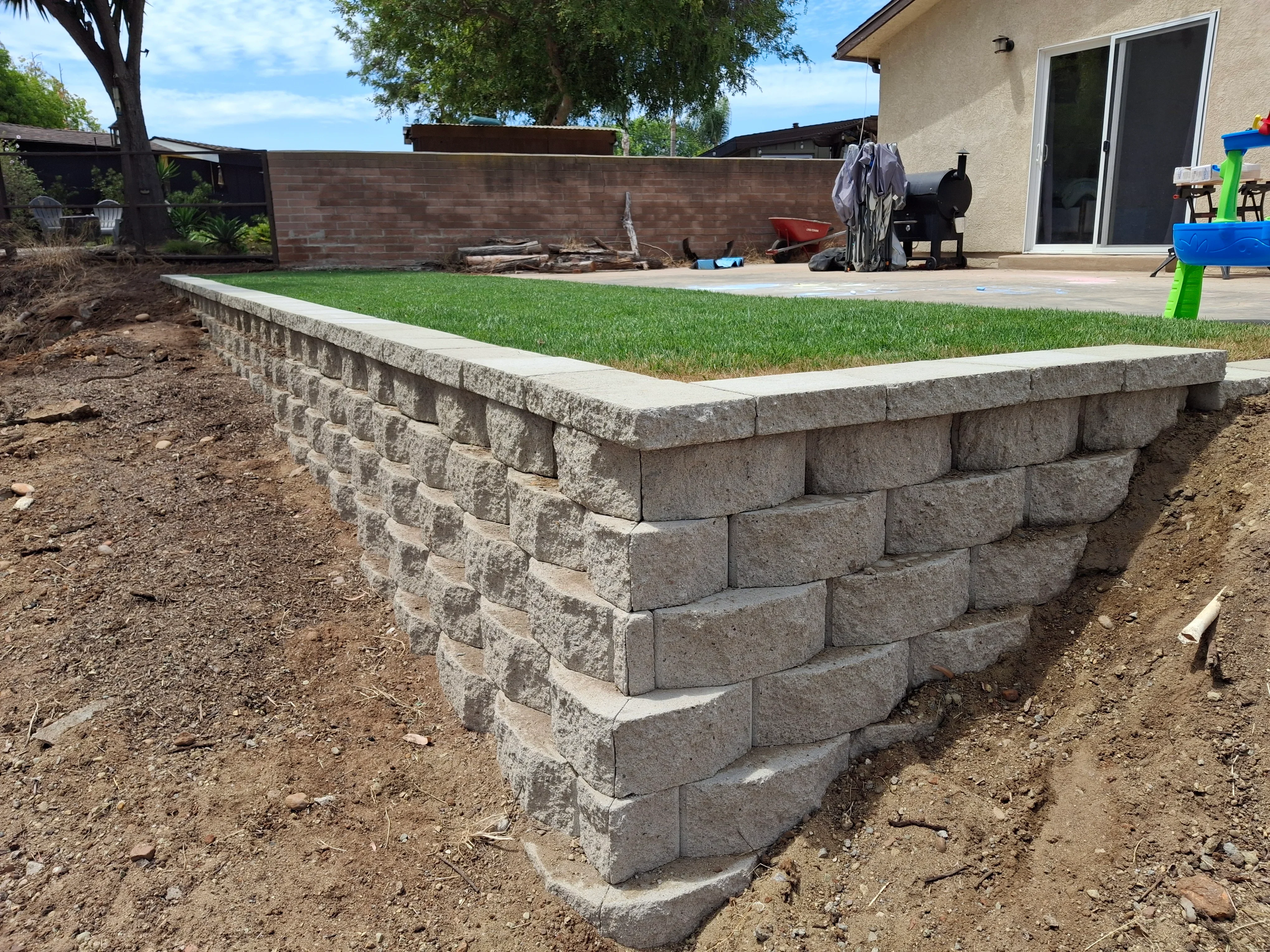 Stacked concrete block retaining wall with finished cap and newly sodded raised lawn area