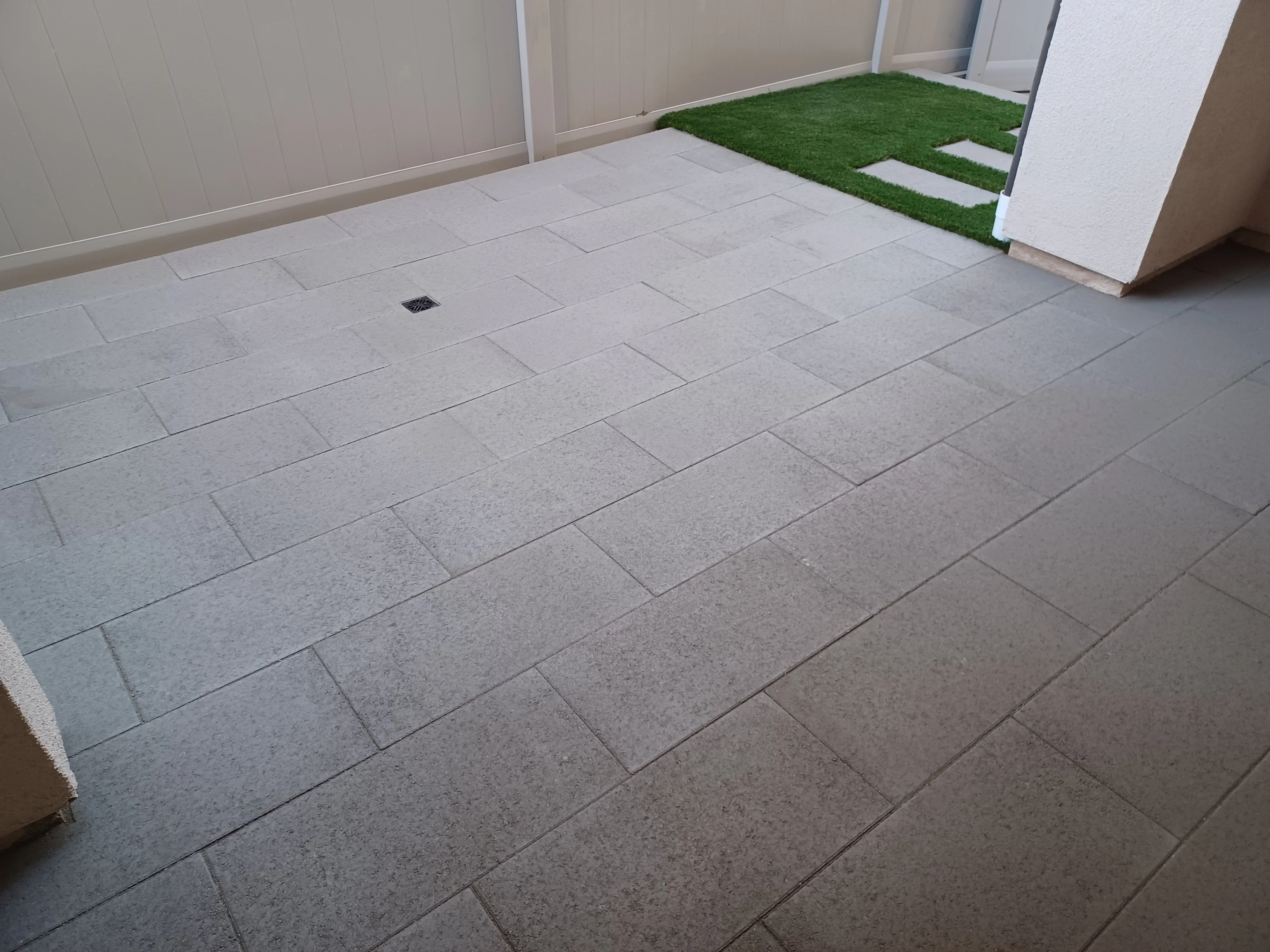 Herringbone patterned concrete pavers with drainage inlet and artificial turf transition