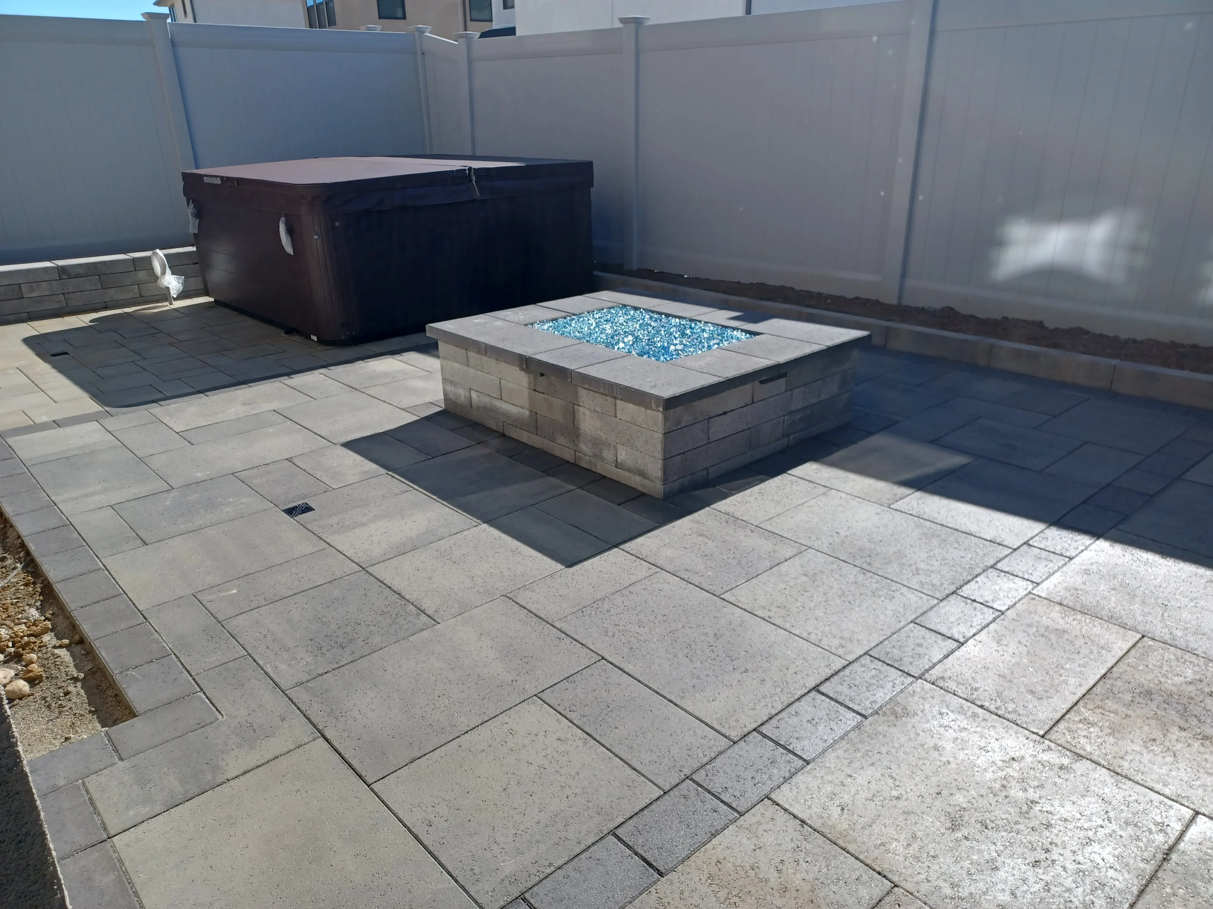 Concrete paver patio with stone-built fire pit filled with blue glass, vinyl fencing backdrop