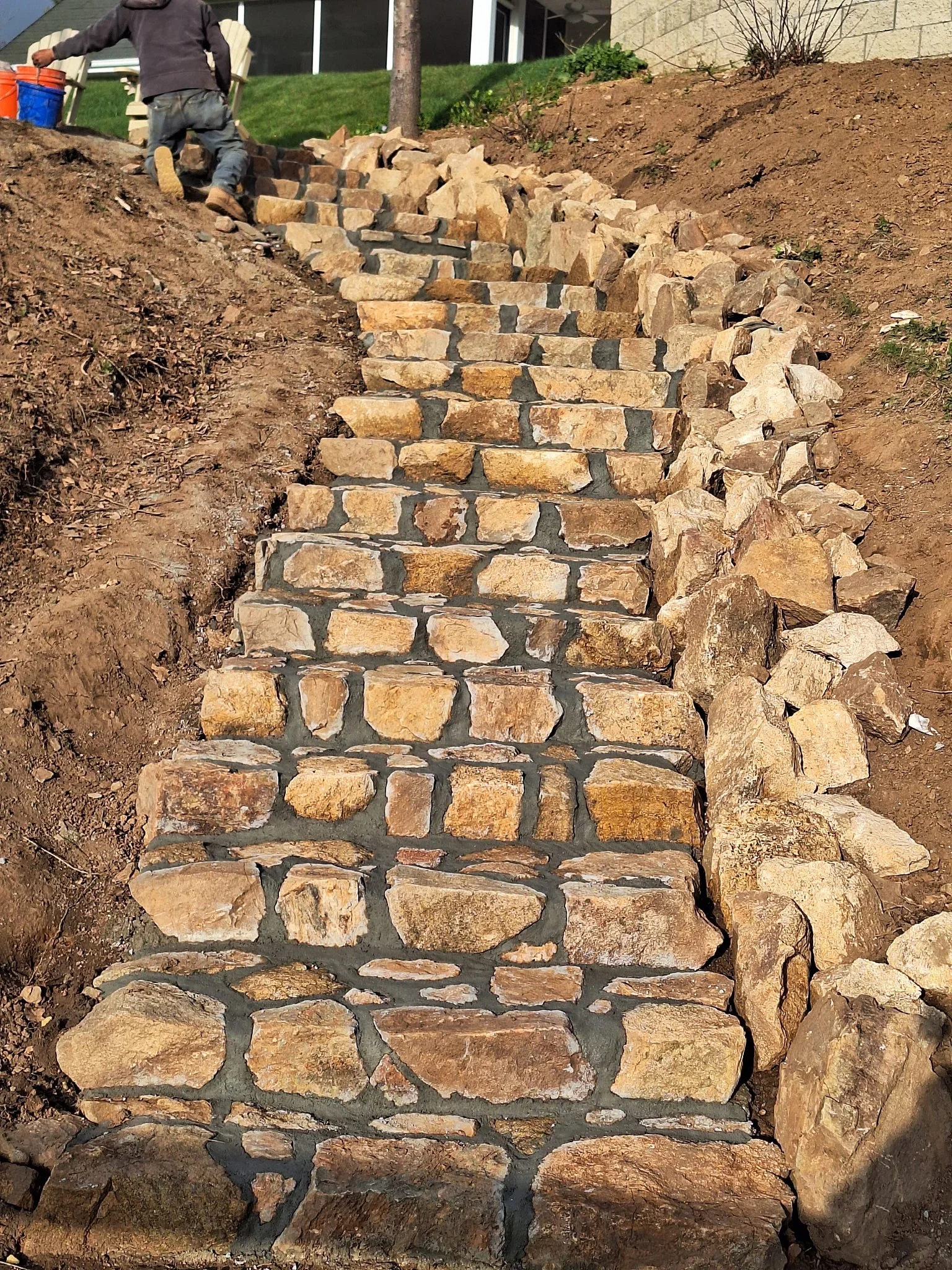 Stacked natural stone retaining wall with mortar joints and integrated stone steps on sloped terrain