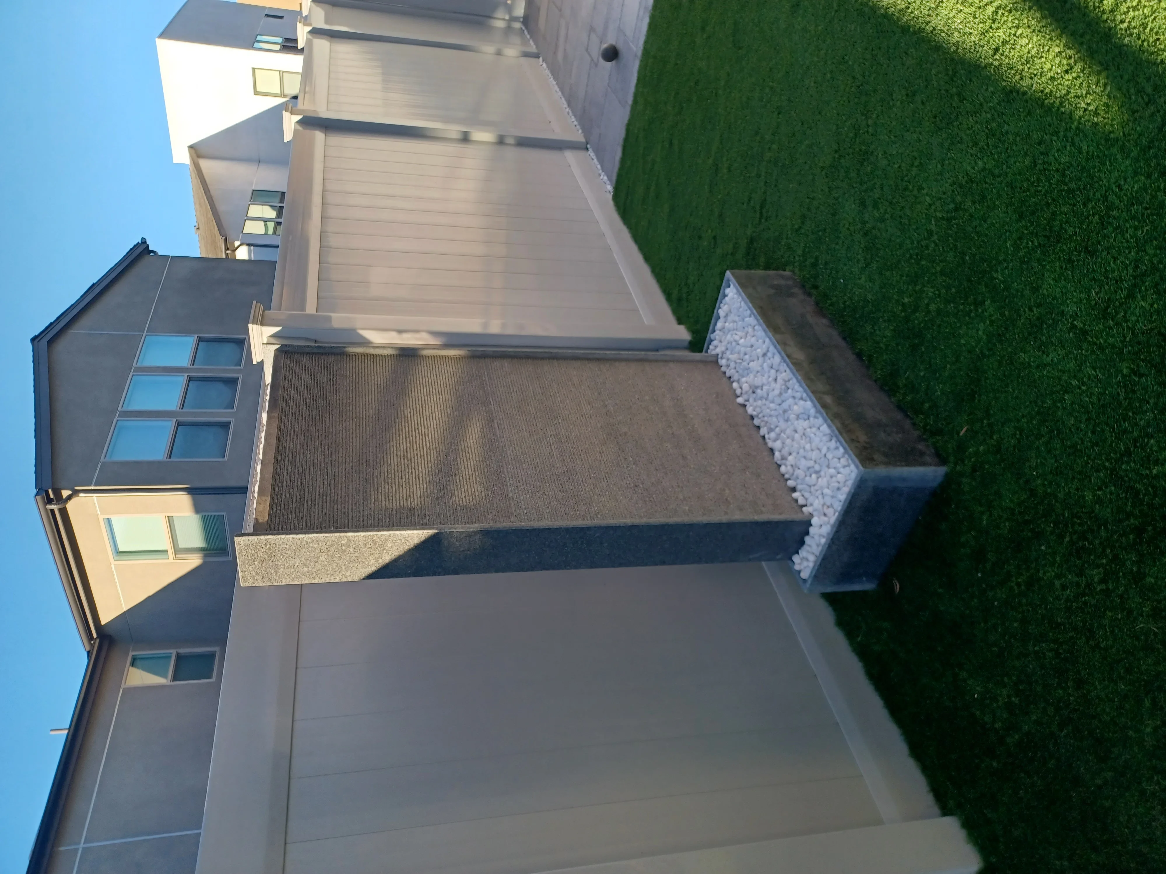 Asphalt driveway with concrete borders, gravel edging, and white stone retaining wall
