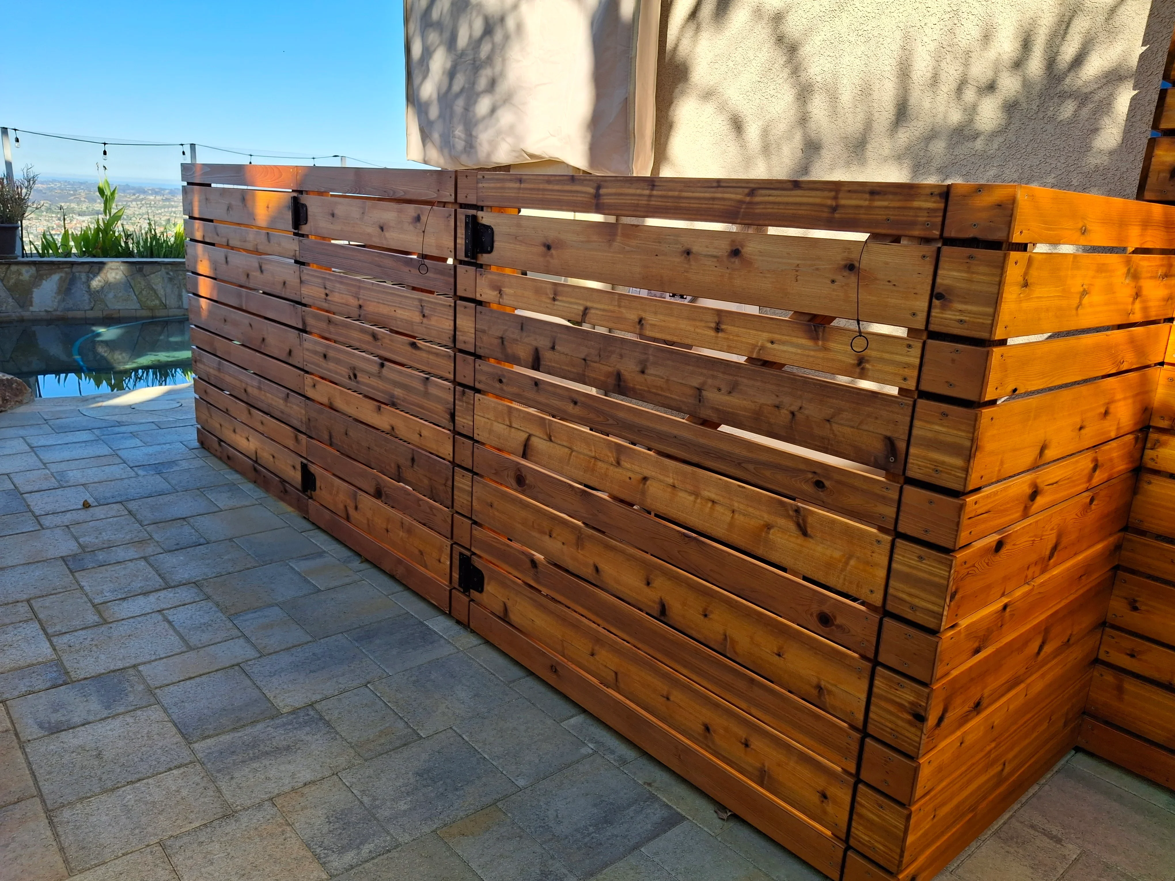 Horizontal wood privacy screen with stained timber planks and metal frame on paved patio