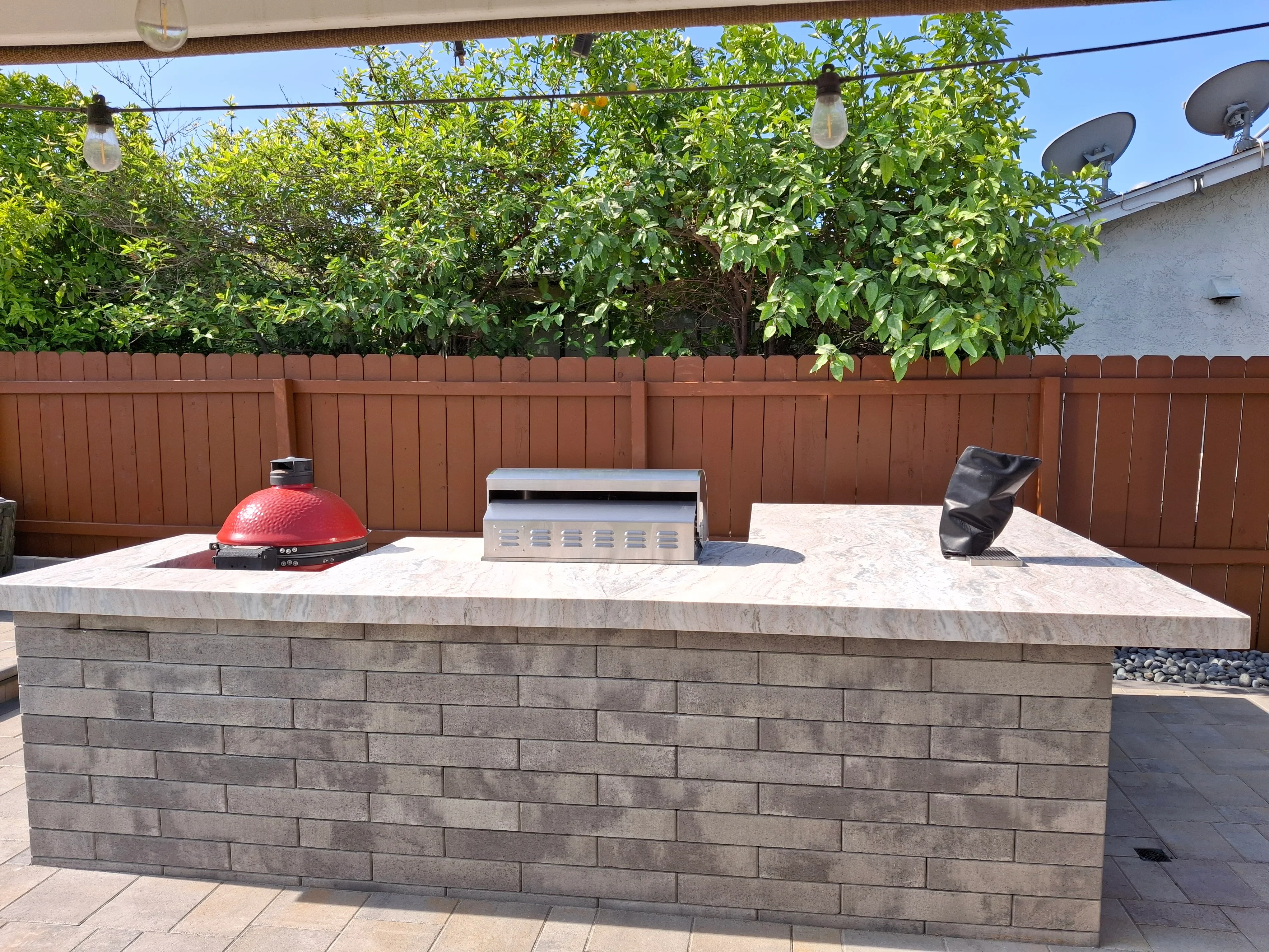 Concrete block outdoor kitchen island with polished countertop, grill, and cooktop on paver patio