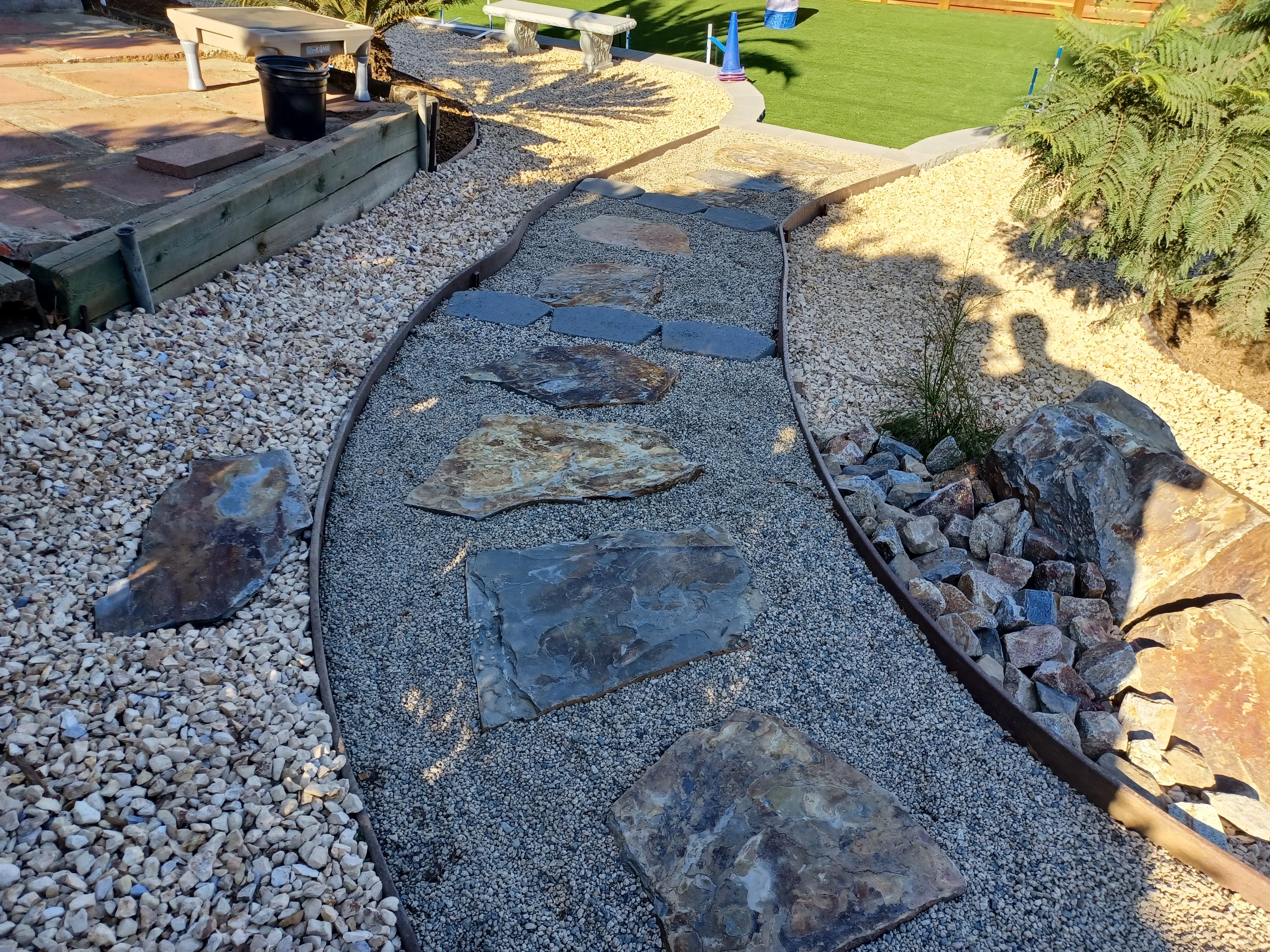 Slate stepping stone pathway with black edging, gravel base, and decorative river rock borders in residential yard