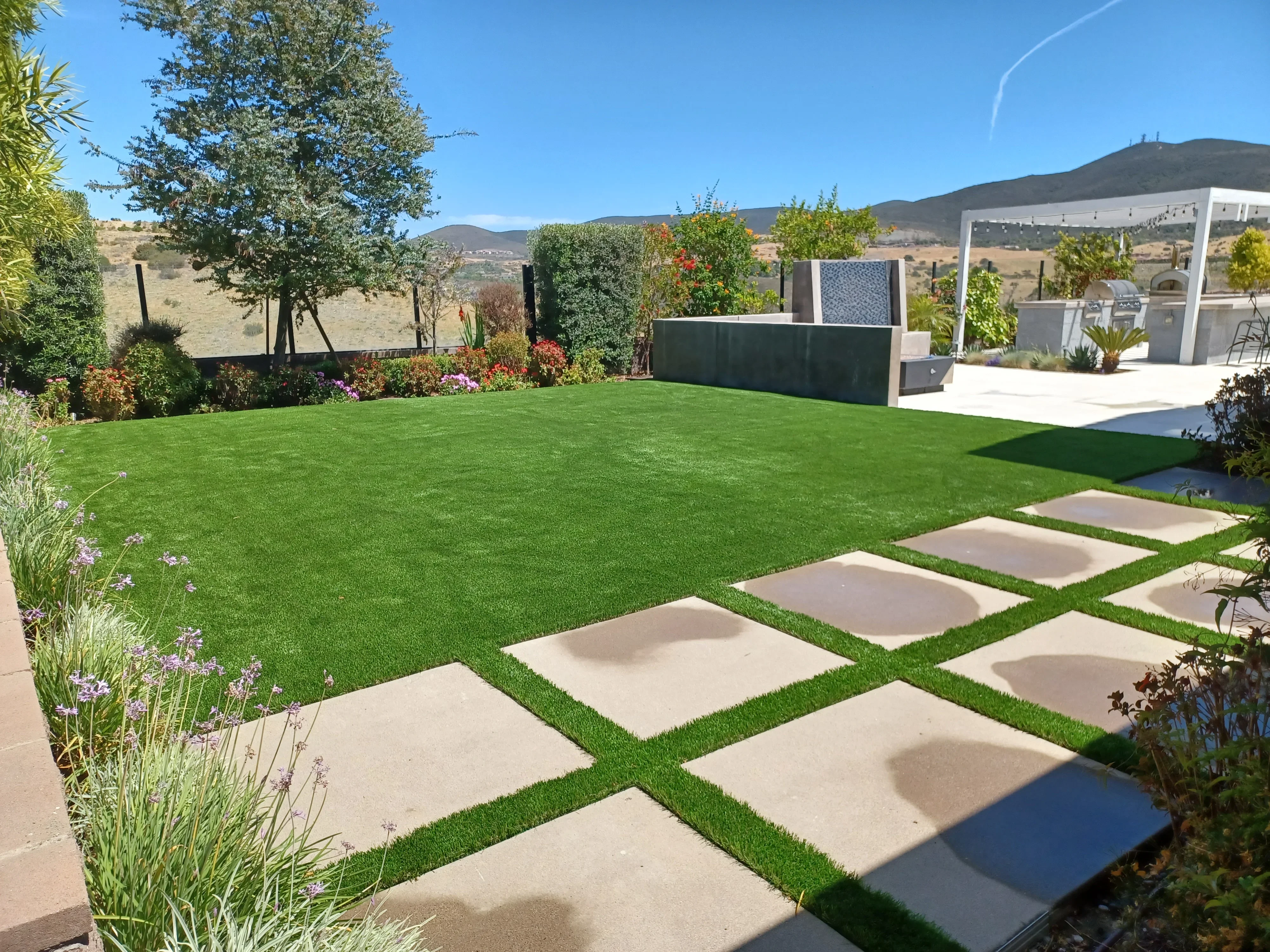 Concrete stepping stones through synthetic turf lawn with modern hardscape patio and metal screens