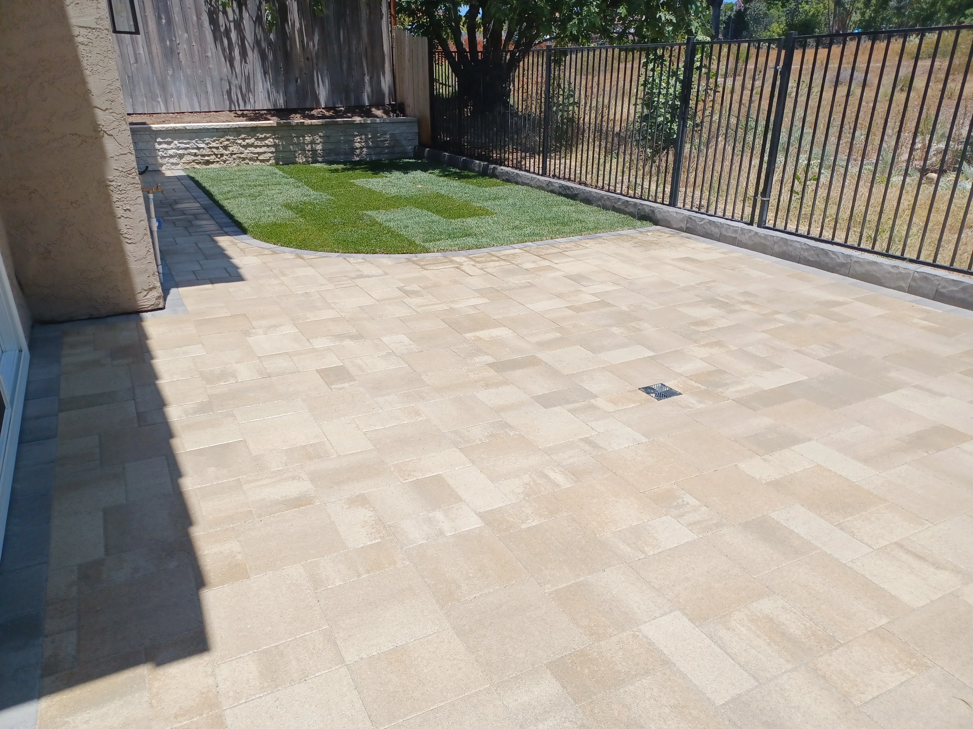 Stone paver patio with running bond pattern, new lawn, concrete retaining wall, and black metal fence