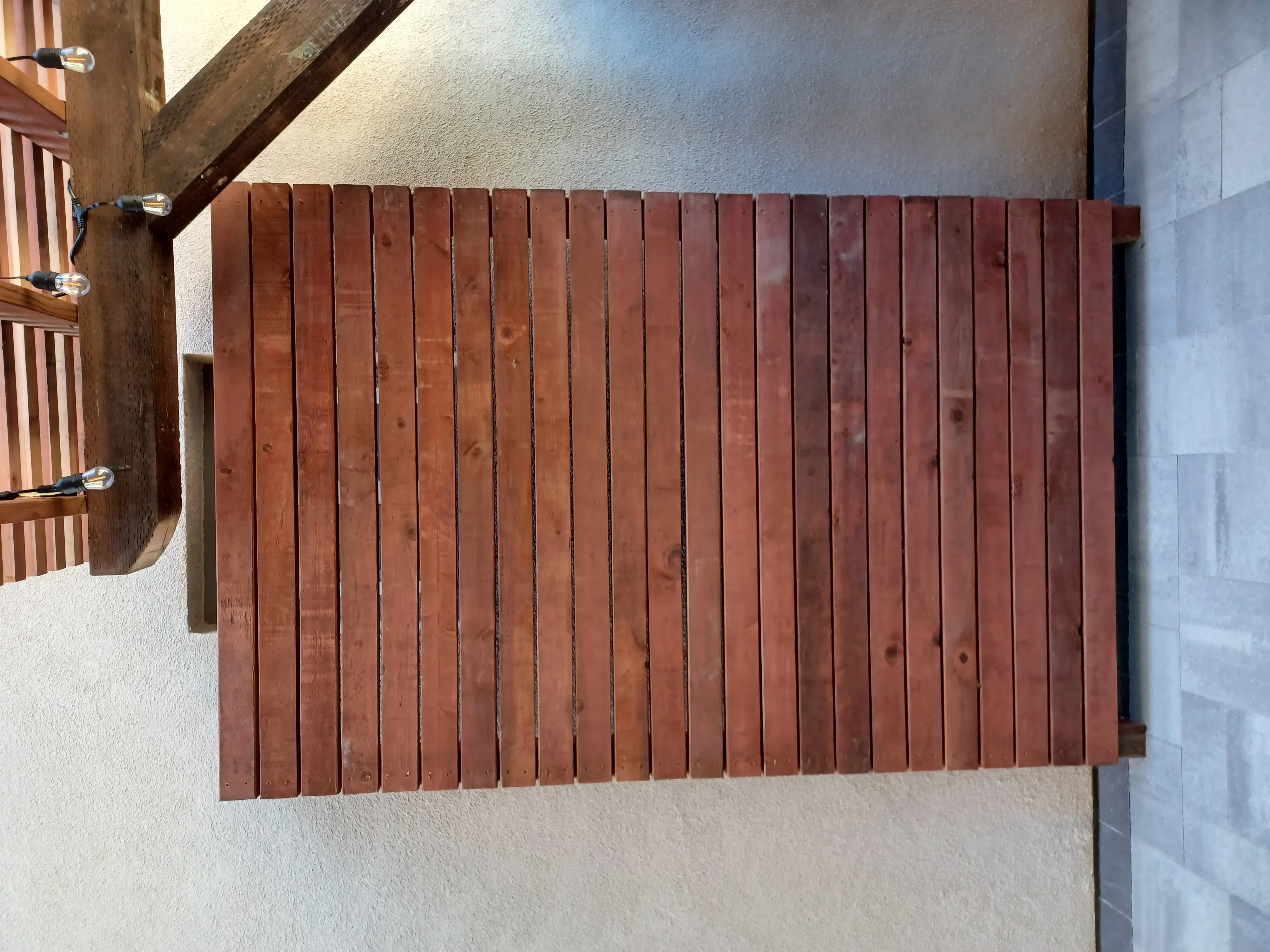 Vertical wood slat privacy screen with evenly spaced boards mounted on stucco wall