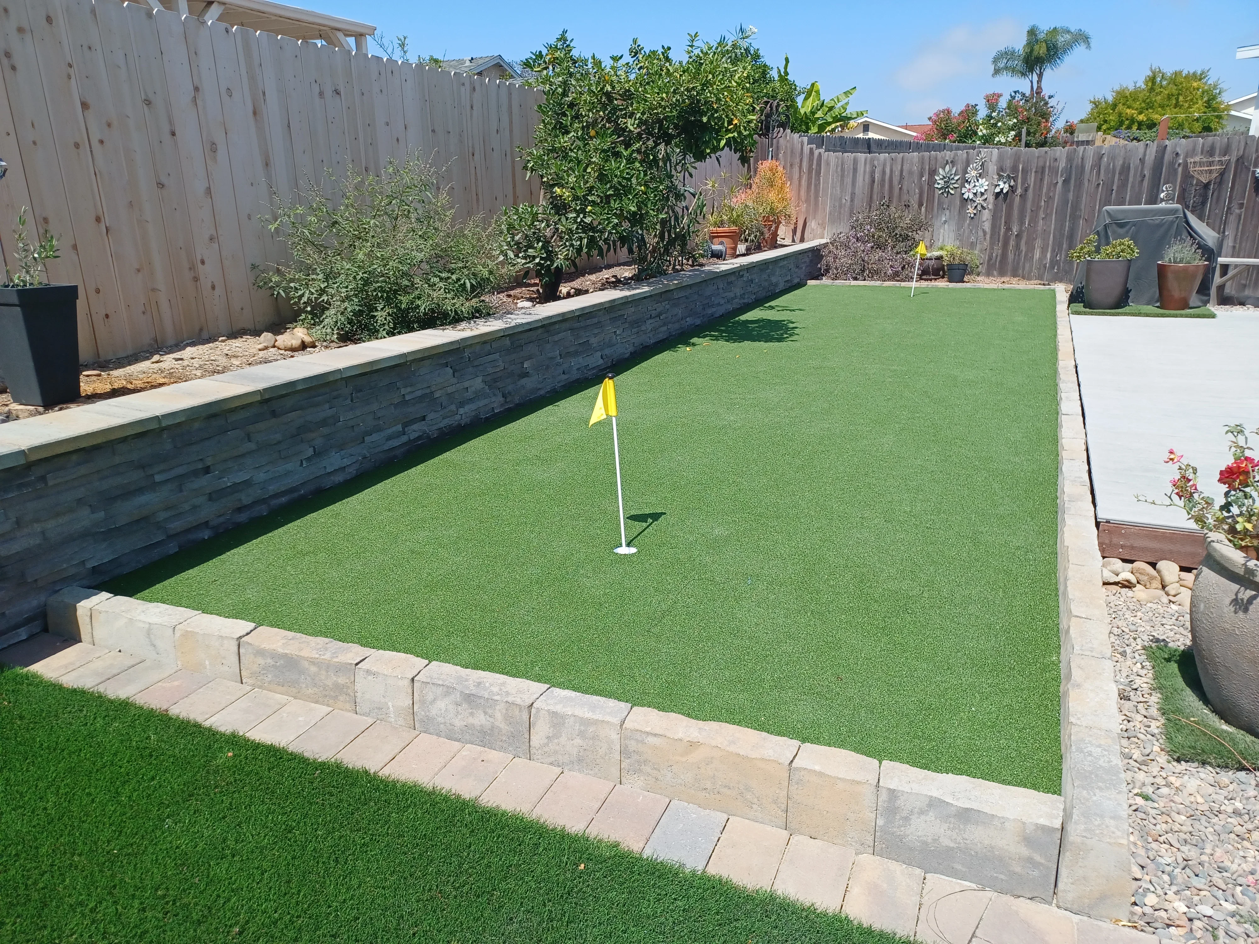 Synthetic putting green with concrete retaining walls, stone edging, and raised planting beds