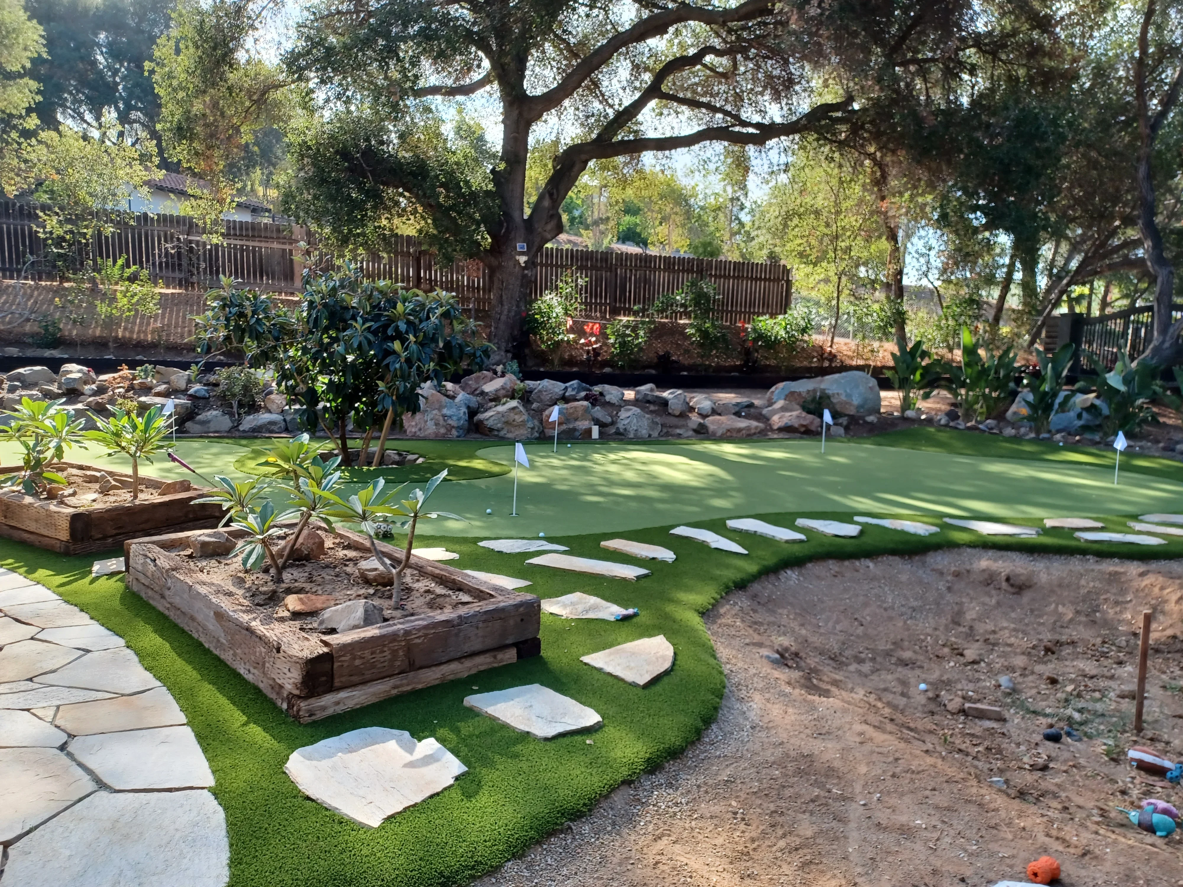 Synthetic putting green with stone steppers, flagstone patio, boulder borders, and timber planters