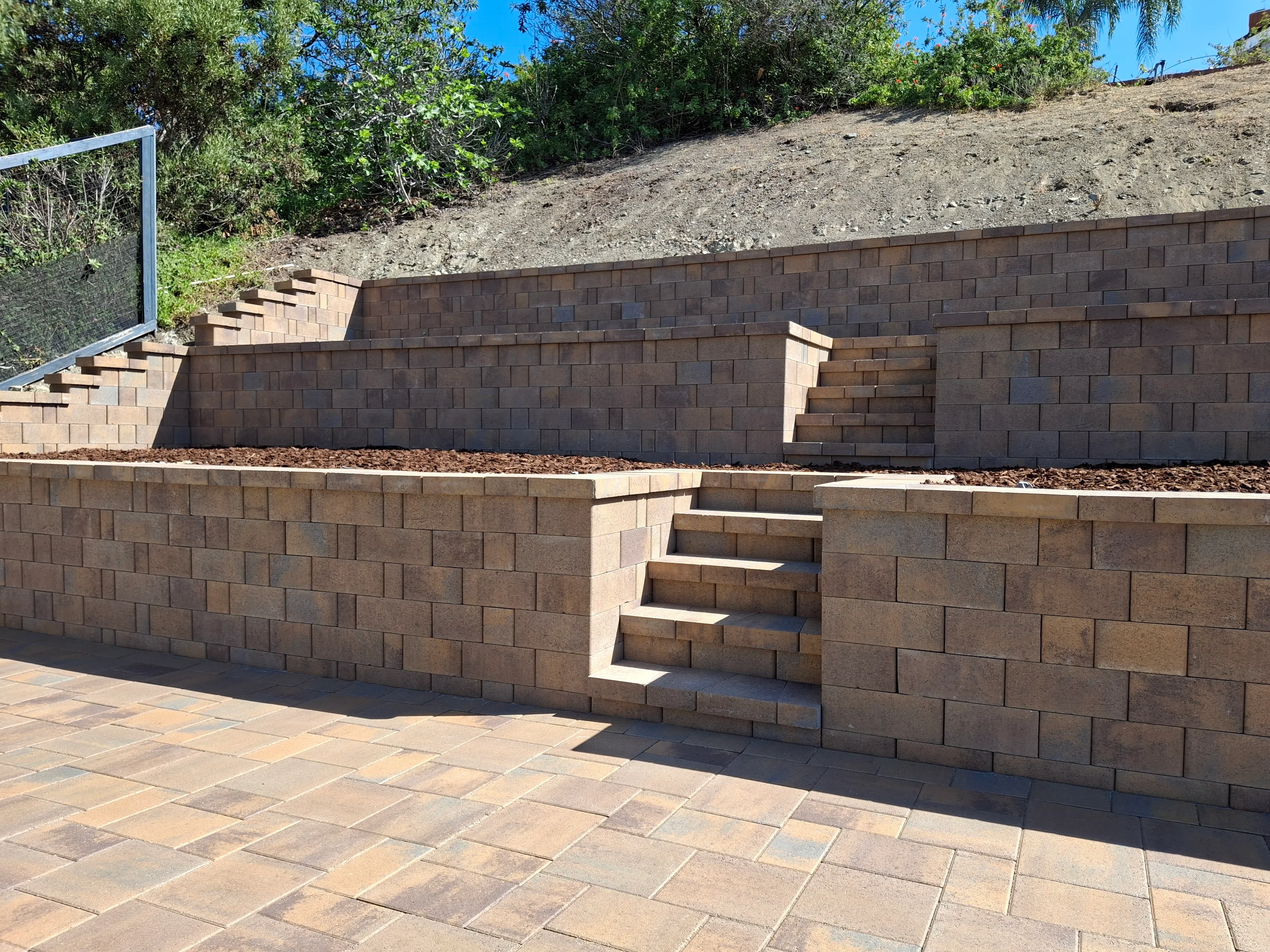 Brown concrete block retaining walls with integrated concrete stairs and paver patio base