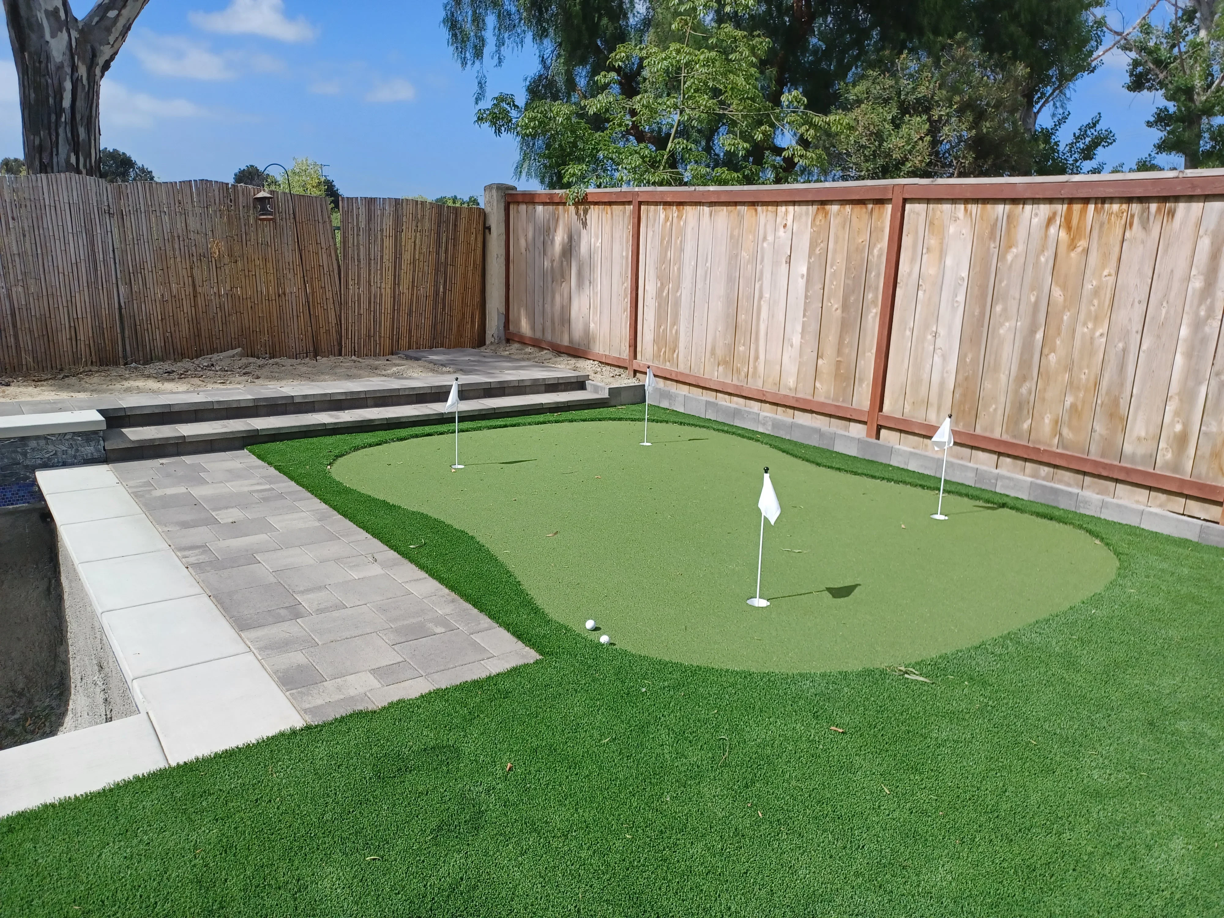Synthetic putting green with paver patio, concrete retaining walls, and wooden privacy fence