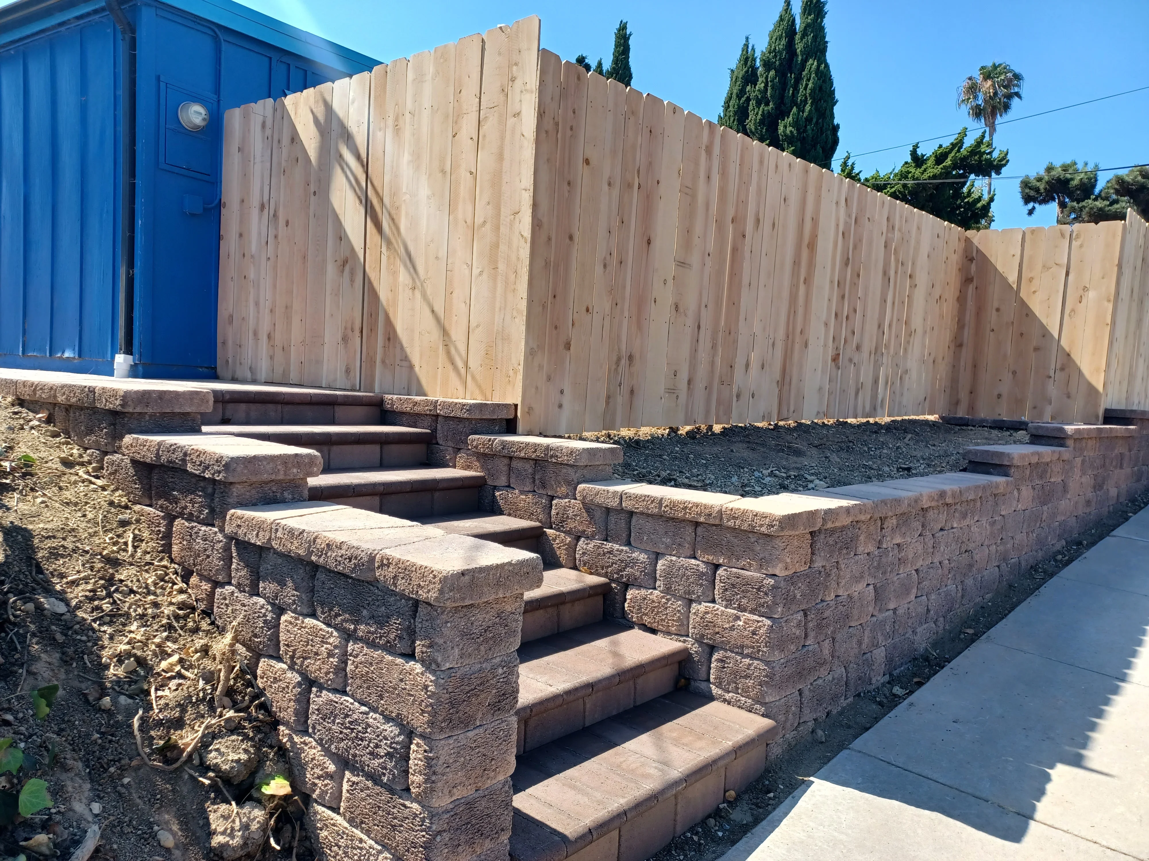Stacked concrete retaining wall with integrated steps and timber fence above
