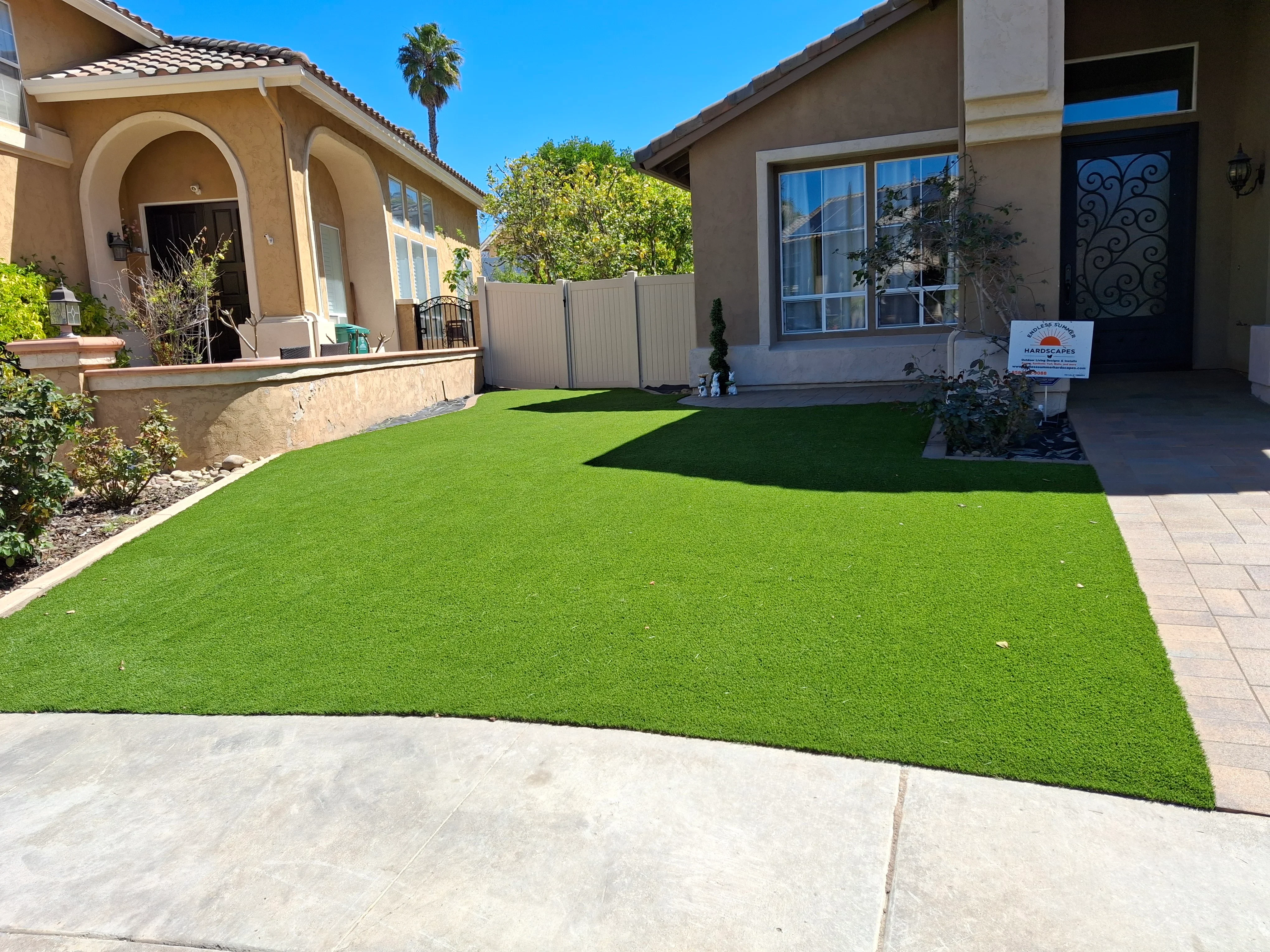 Synthetic turf lawn with concrete pavers and metal fence in residential backyard