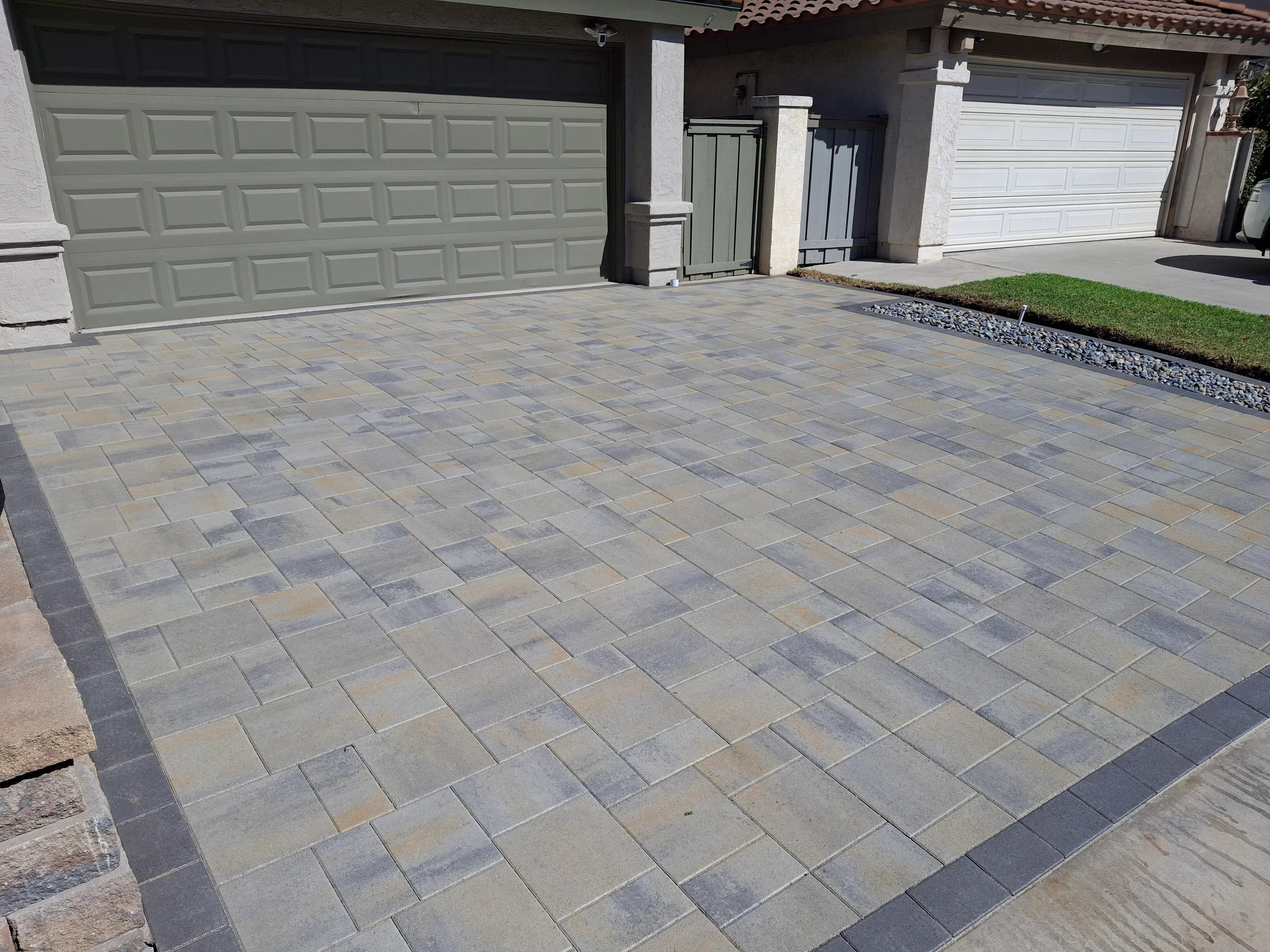 Multi-colored permeable concrete pavers installed in running bond pattern with dark border edging on residential driveway