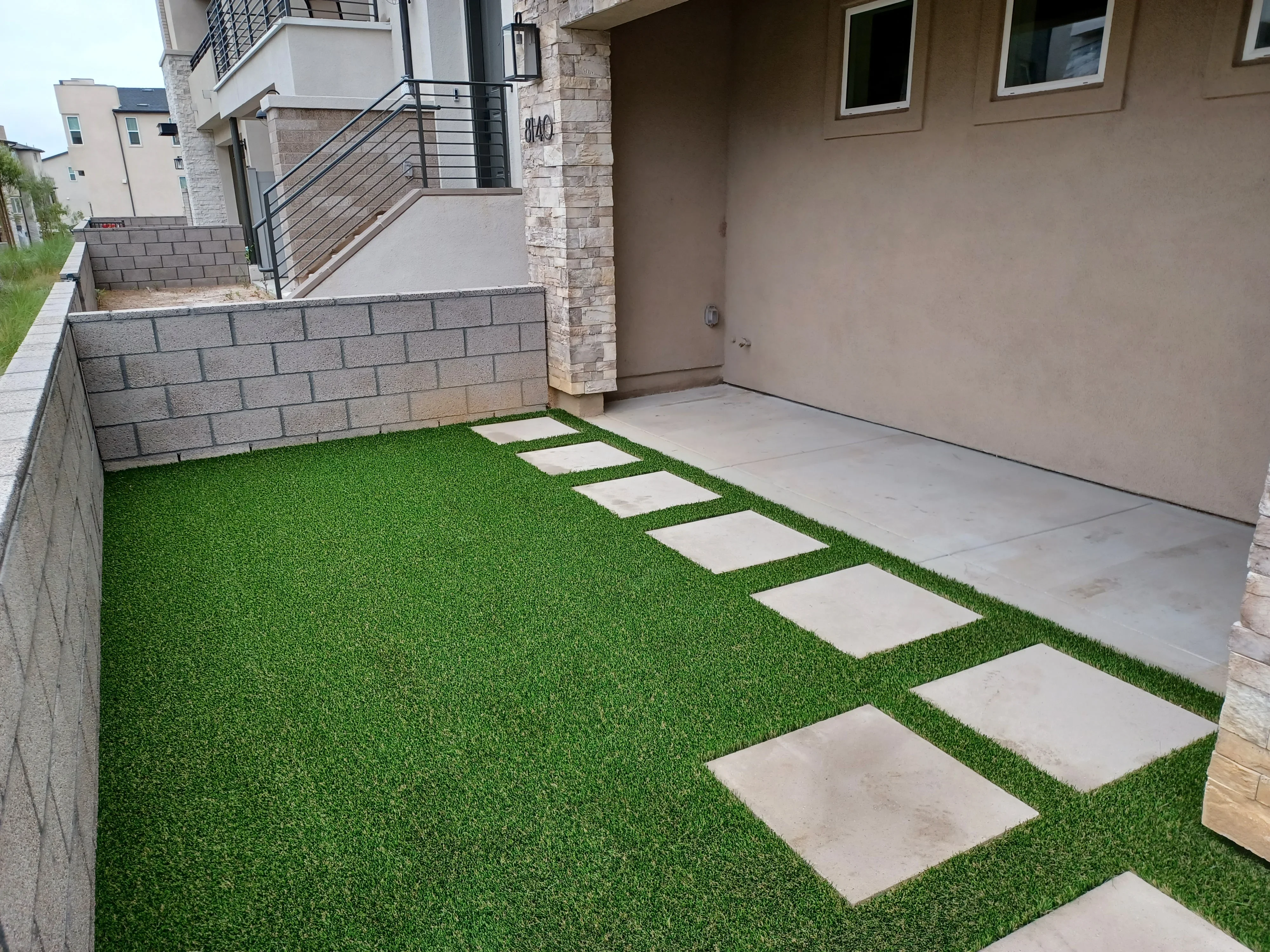 Synthetic turf yard with concrete stepping stone pathway and retaining wall